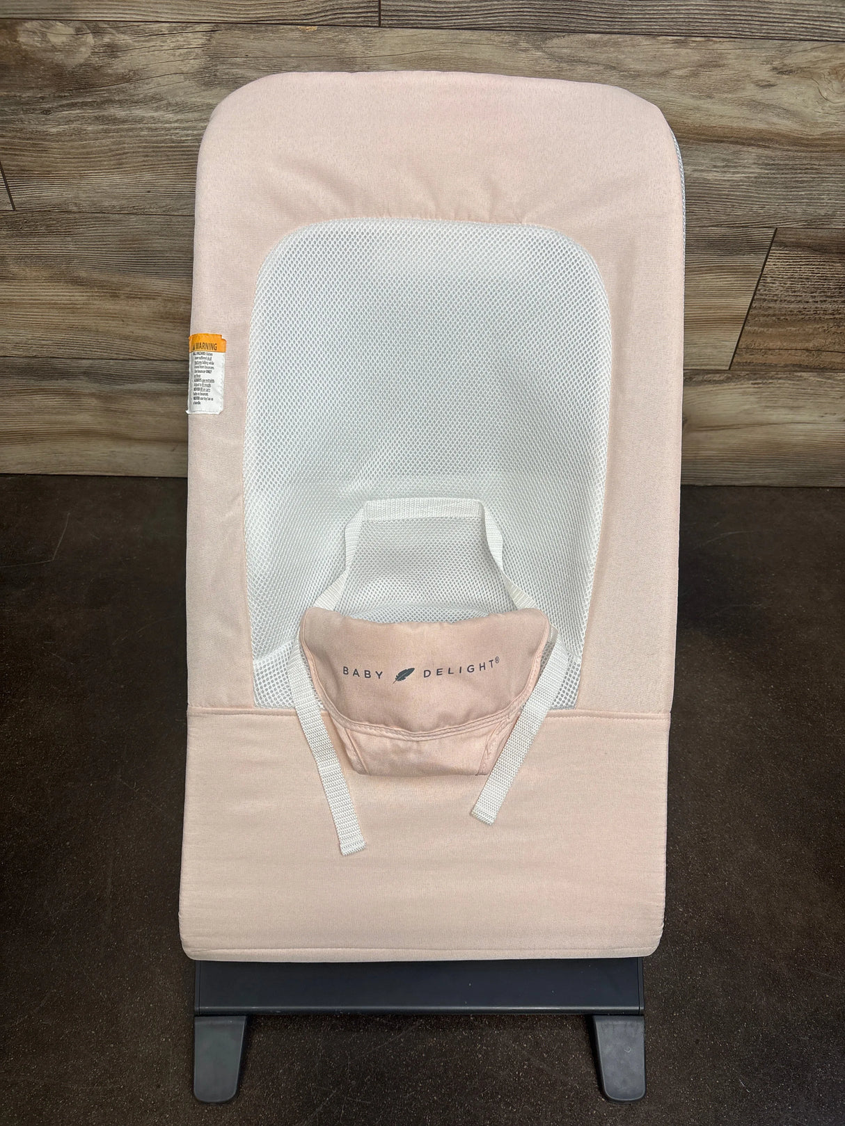 Top-down view of Baby Delight Alpine Deluxe bouncer in light pink showing white mesh seat insert, safety straps, and black base on wood floor