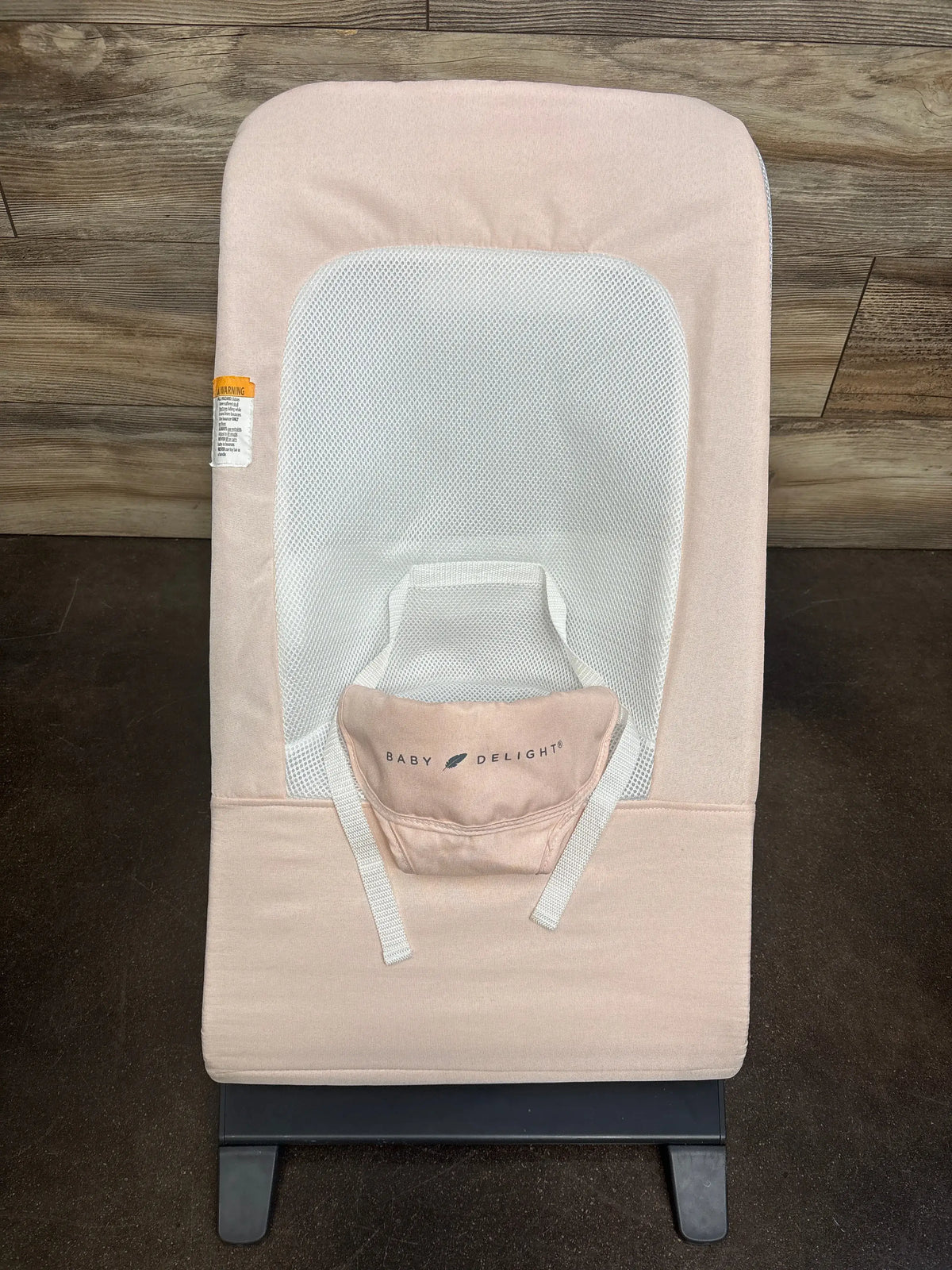 Top-down view of Baby Delight Alpine Deluxe bouncer in light pink showing white mesh seat insert, safety straps, and black base on wood floor