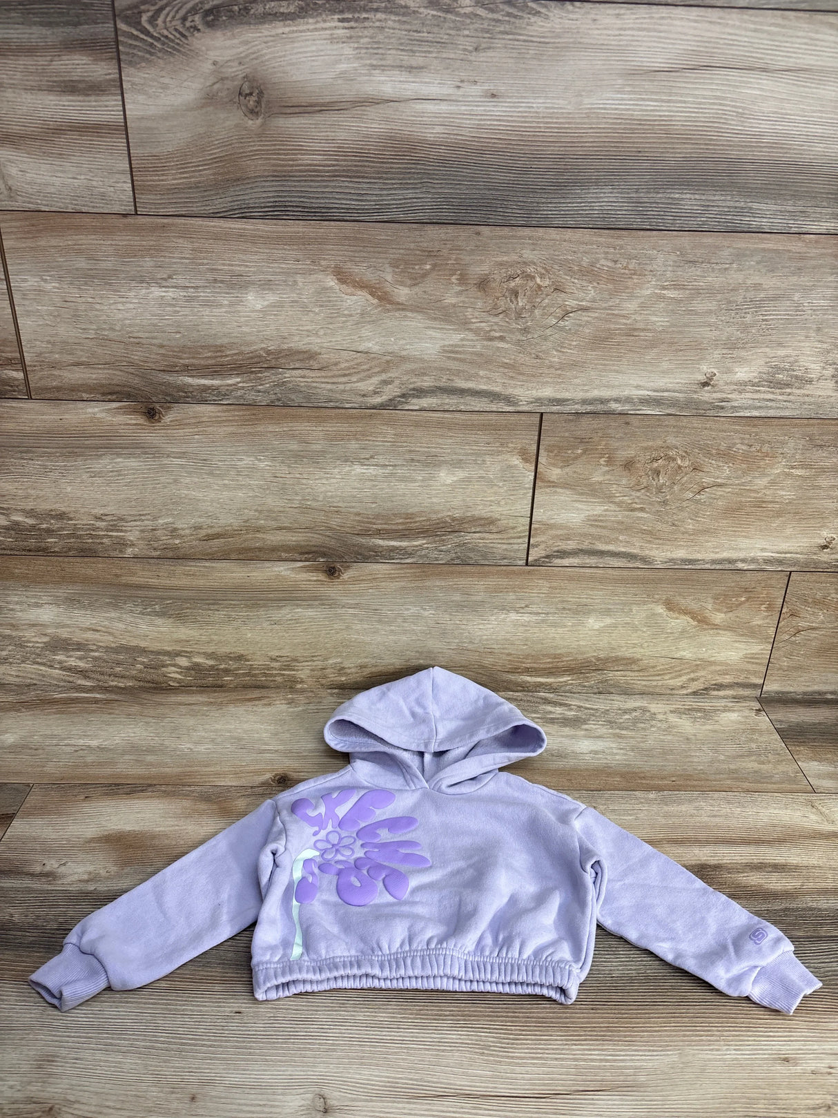 Lavender cropped hoodie with large purple floral graphic on front, laid flat on wooden floor