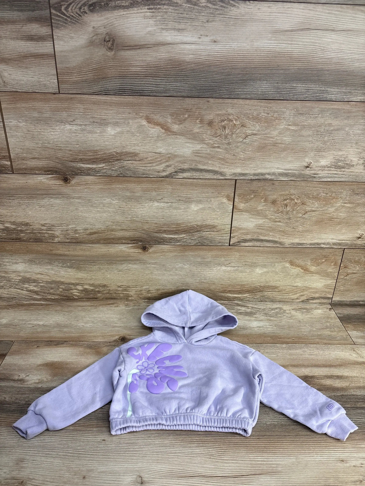Lavender cropped hoodie with large purple floral graphic on front, laid flat on wooden floor