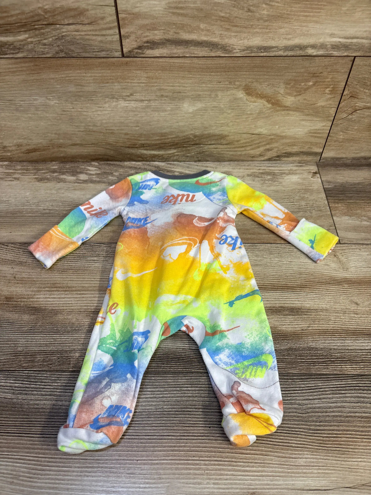 Front view of a Nike newborn sleeper showcasing a multicolor abstract print and covered feet on a wood floor