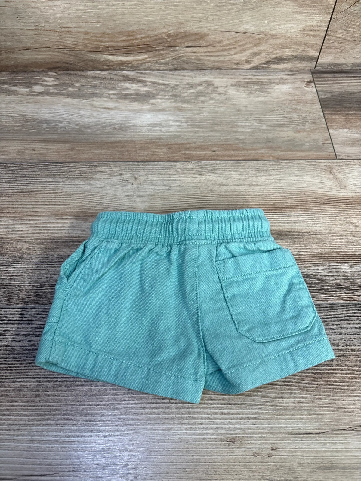 Flat lay of Carter’s Shorts in teal with elastic waistband and side pockets on wood plank floor