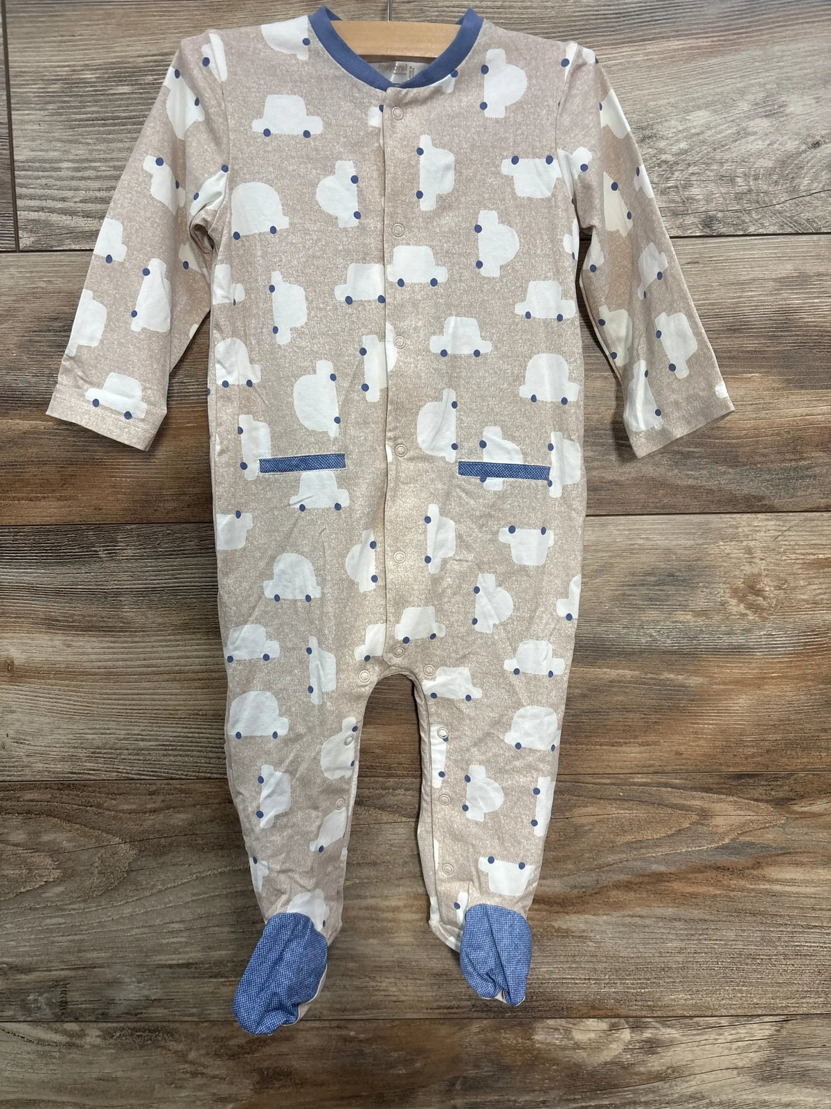 Beige baby onesie with white car prints, blue collar and footed legs on wooden floor
