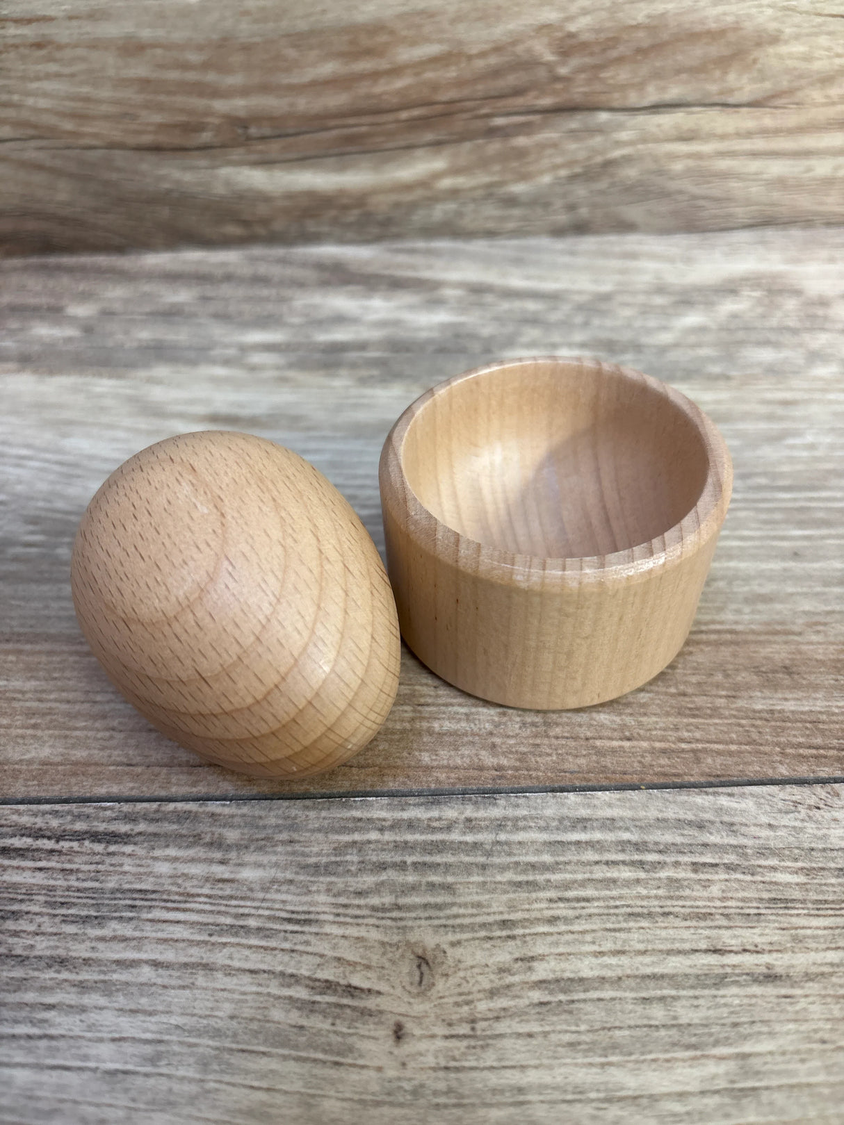 Natural wood egg-shaped container with removable lid on rustic wooden surface