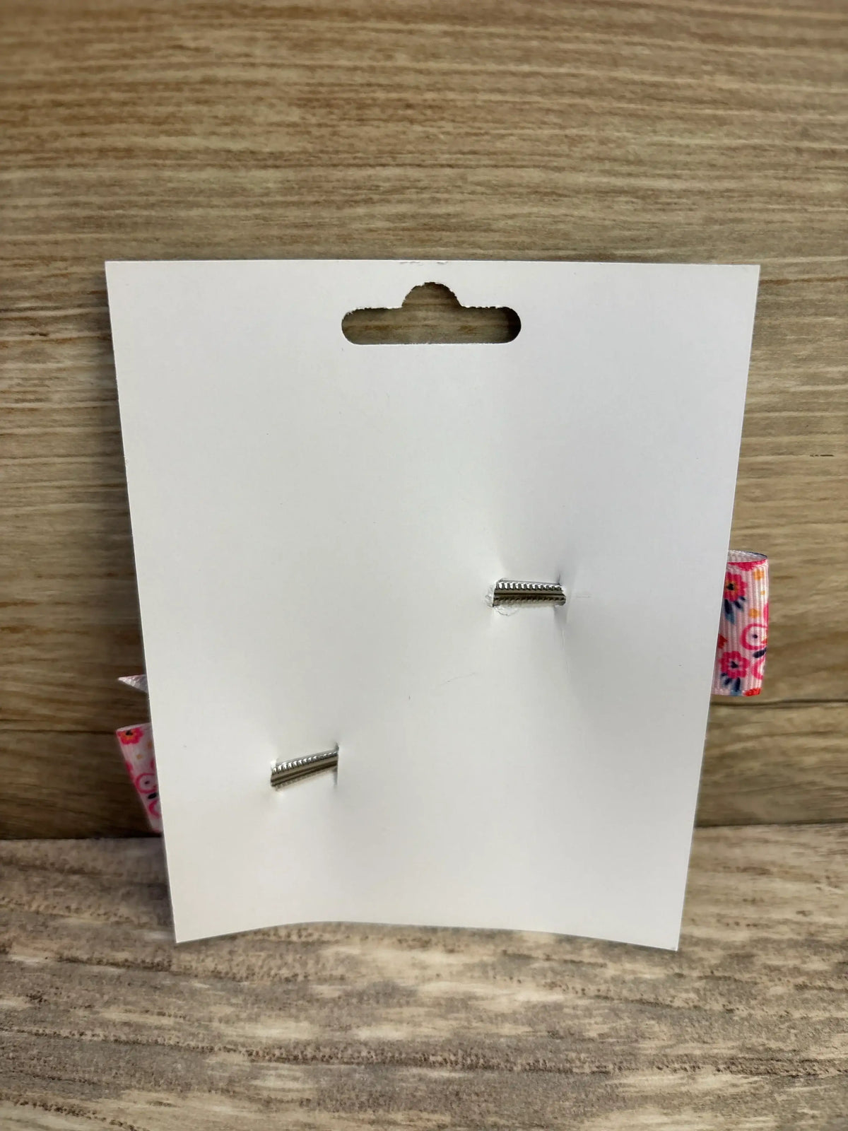 Rear view of two pink butterfly fanned-out hair bows clipped to a white display card on a wood surface