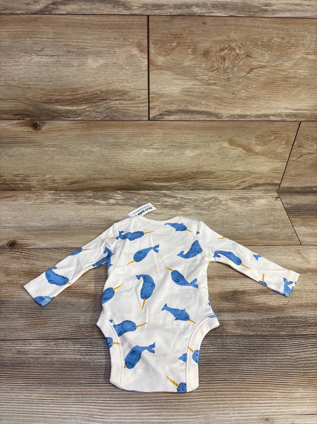 Flat lay of ivory long-sleeve baby bodysuit with blue narwhal print on wood background