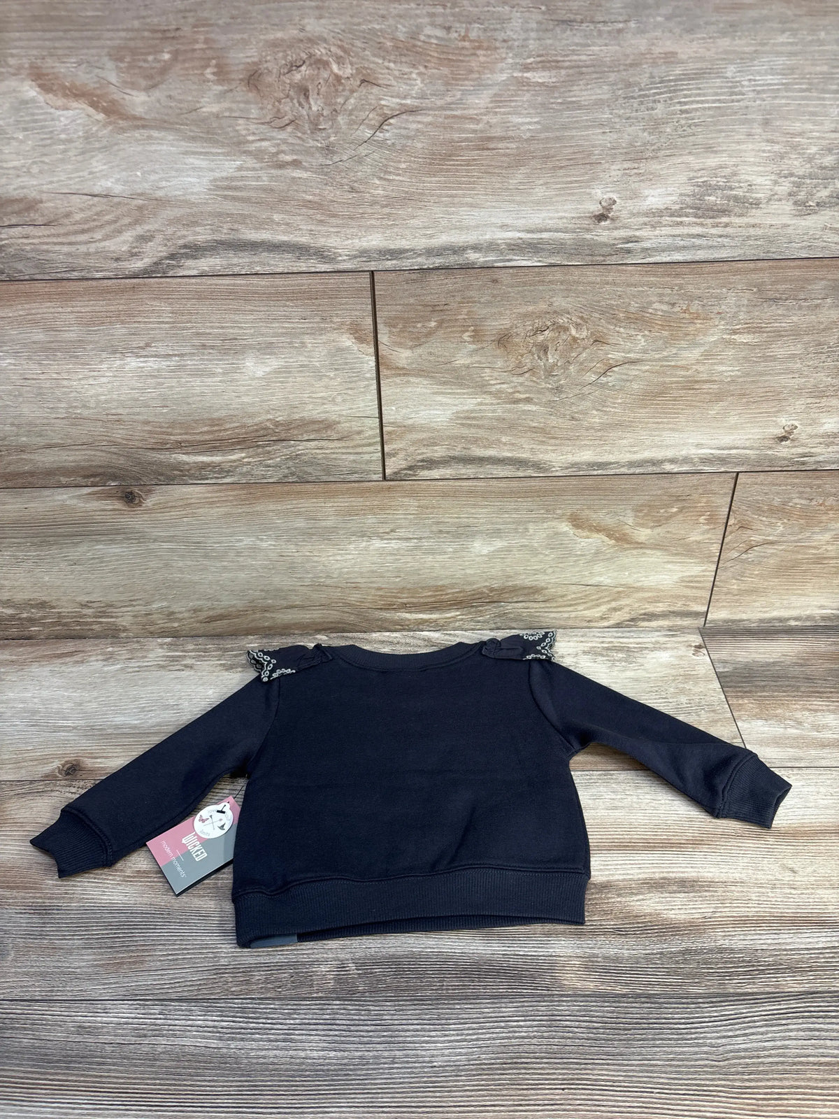 Front view of grey Modern Moments x Wicked Elphaba sweatshirt showcasing eyelet shoulder ruffles on wood-look background