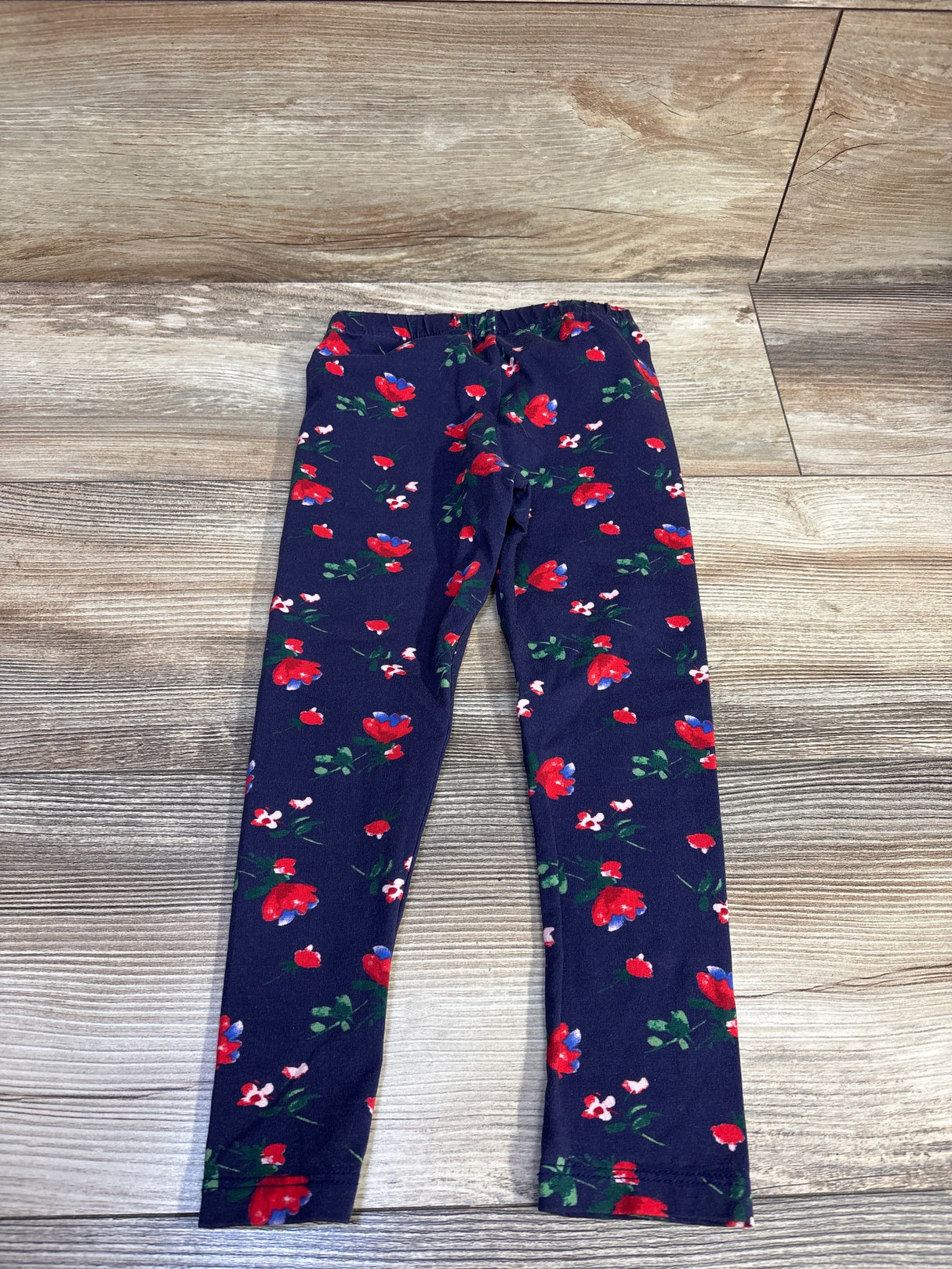 Flat lay of Janie & Jack navy toddler leggings (4T) showing red and pink floral print and elastic waistband on wood background