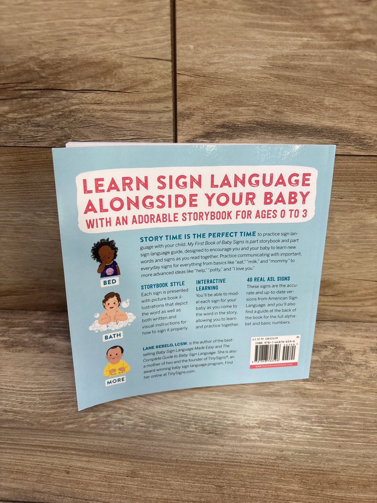 Back cover view of My First Book of Baby Signs Paperback Book showcasing blue cover with Learn Sign Language Alongside Your Baby title and illustrations on wood plank floor
