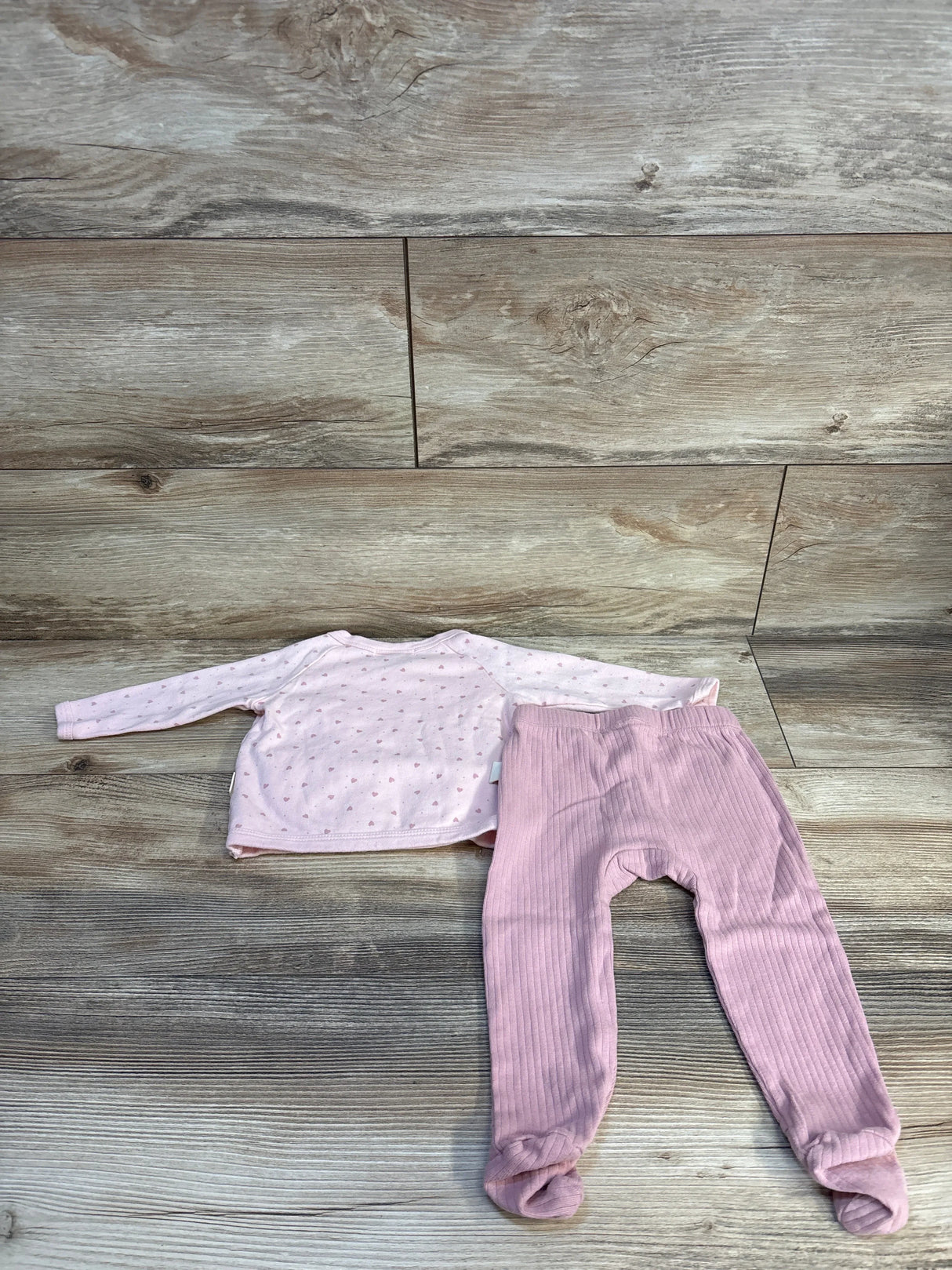 Pink baby long sleeve shirt with heart print and pink footed pants on wooden floor