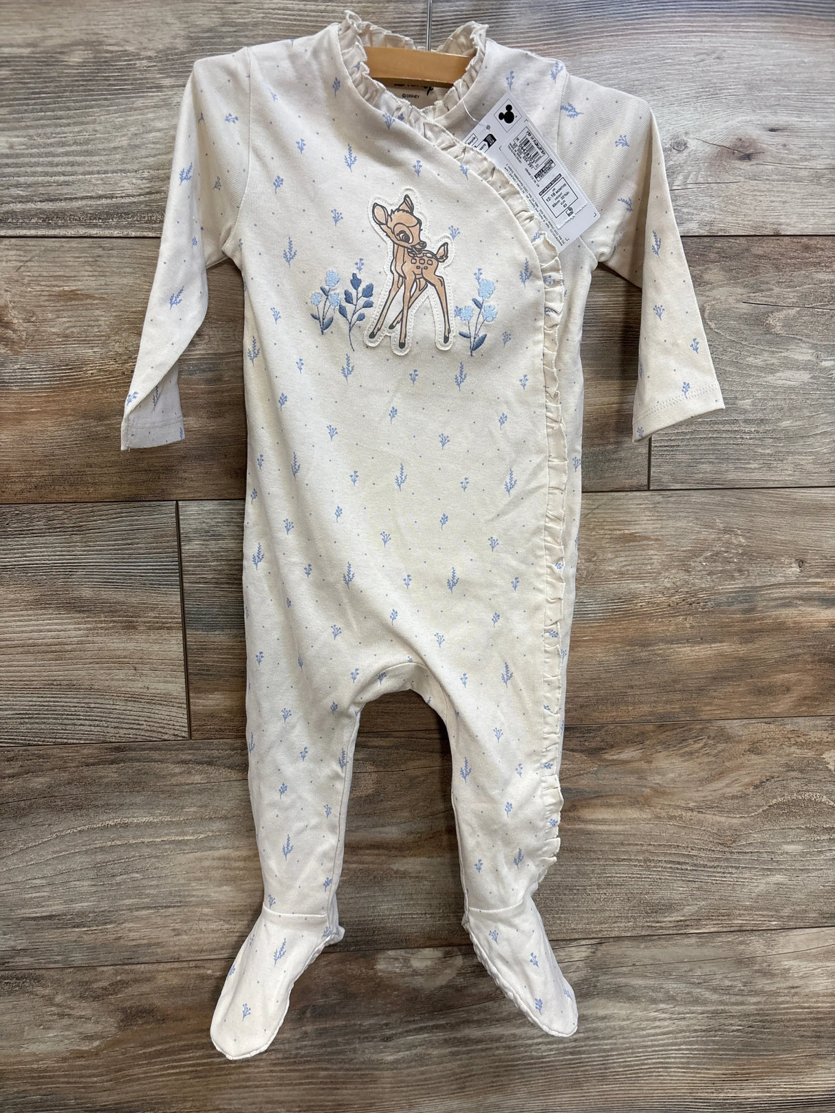 Front view of Disney Bambi footed sleeper with embroidered Bambi, ruffle trim, and pale blue floral print on wood background