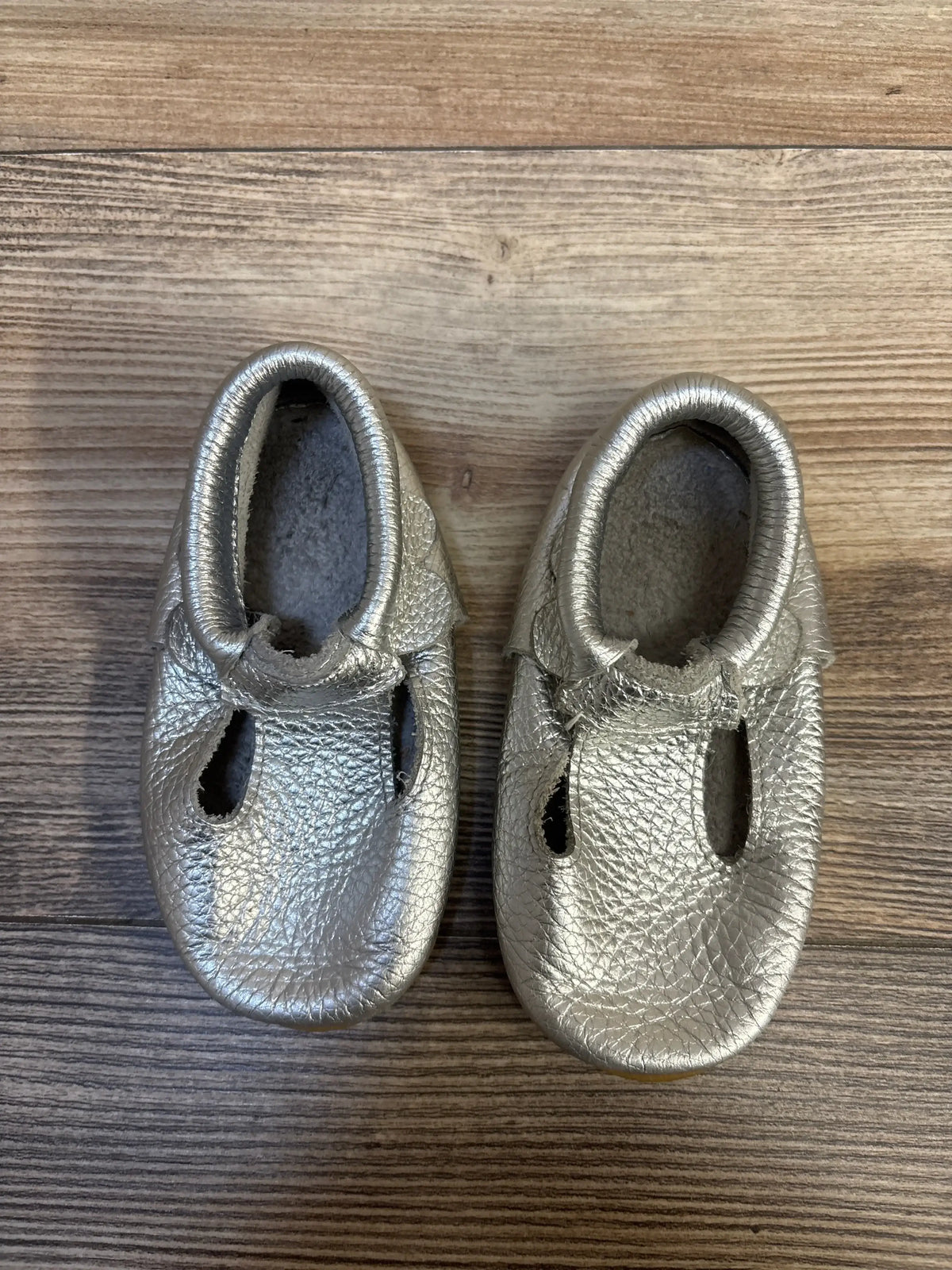 Silver leather baby moccasins on wooden floor, gently used kids shoes.