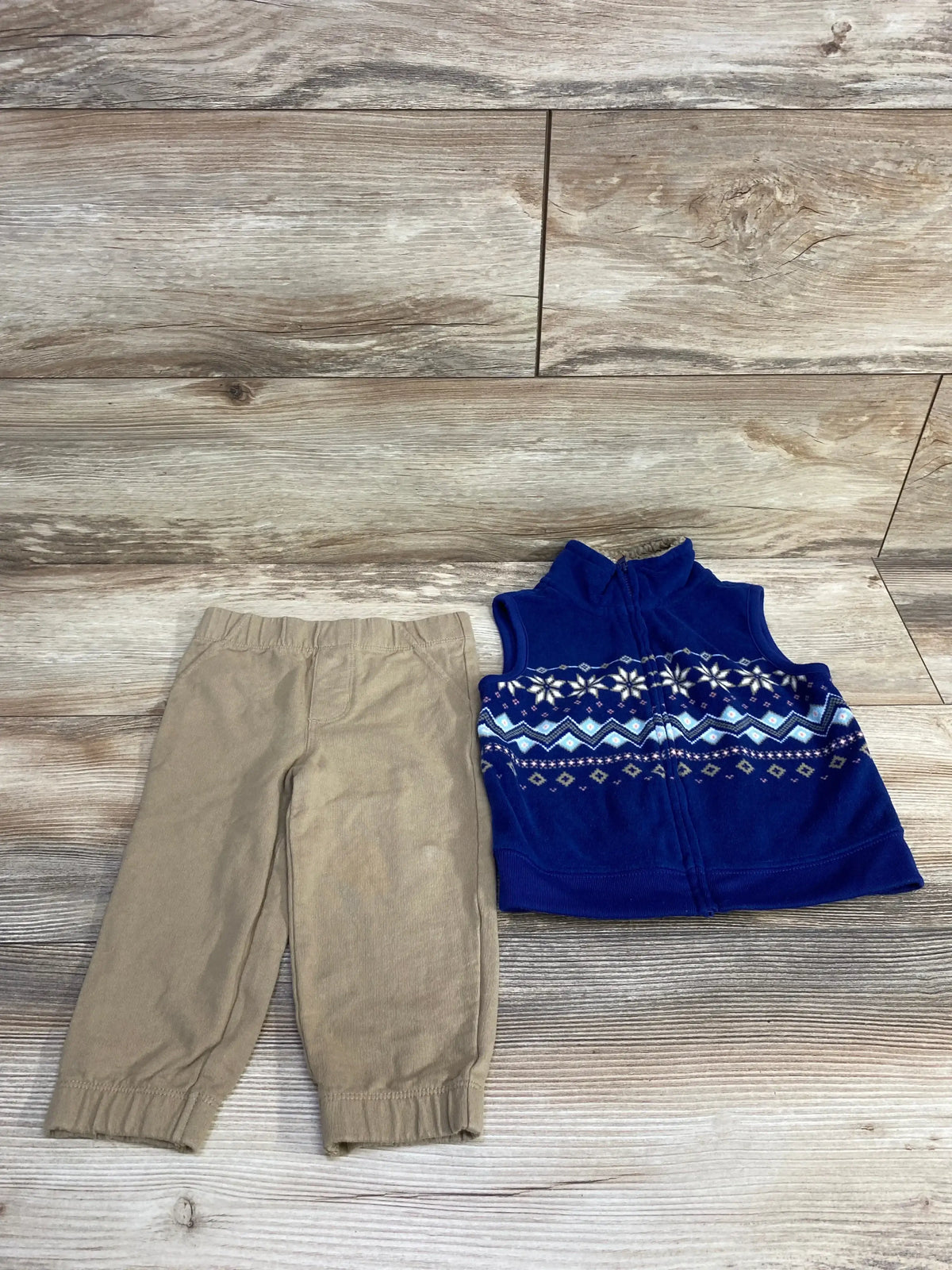 Toddler tan pants and blue fleece vest with snowflake pattern on wood background