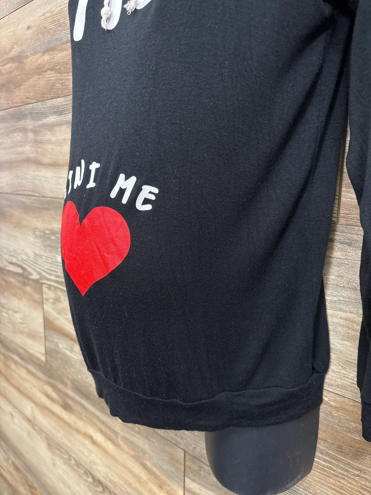 Black maternity shirt with red heart and 'Mini Me' text on mannequin, wood background