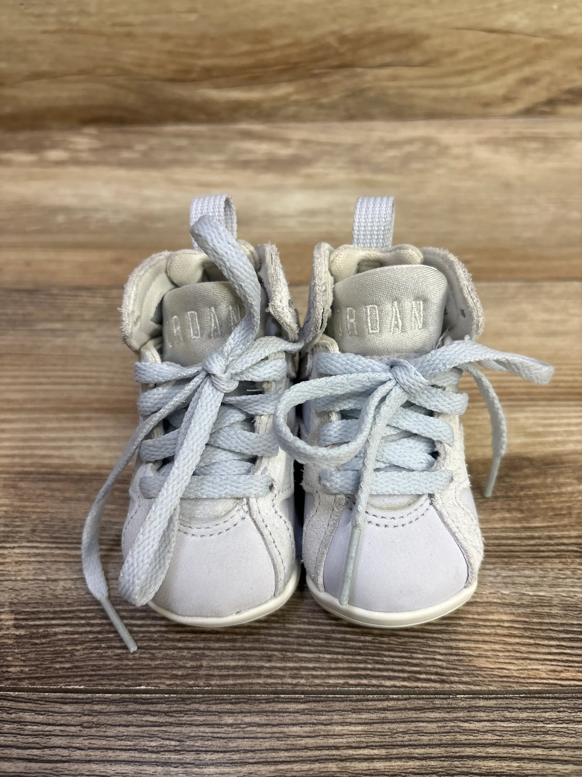 Front view of Air Jordan 7 Retro TD Cobalt Bliss sneakers showing pale blue gray laces and Jordan branding on a wood surface