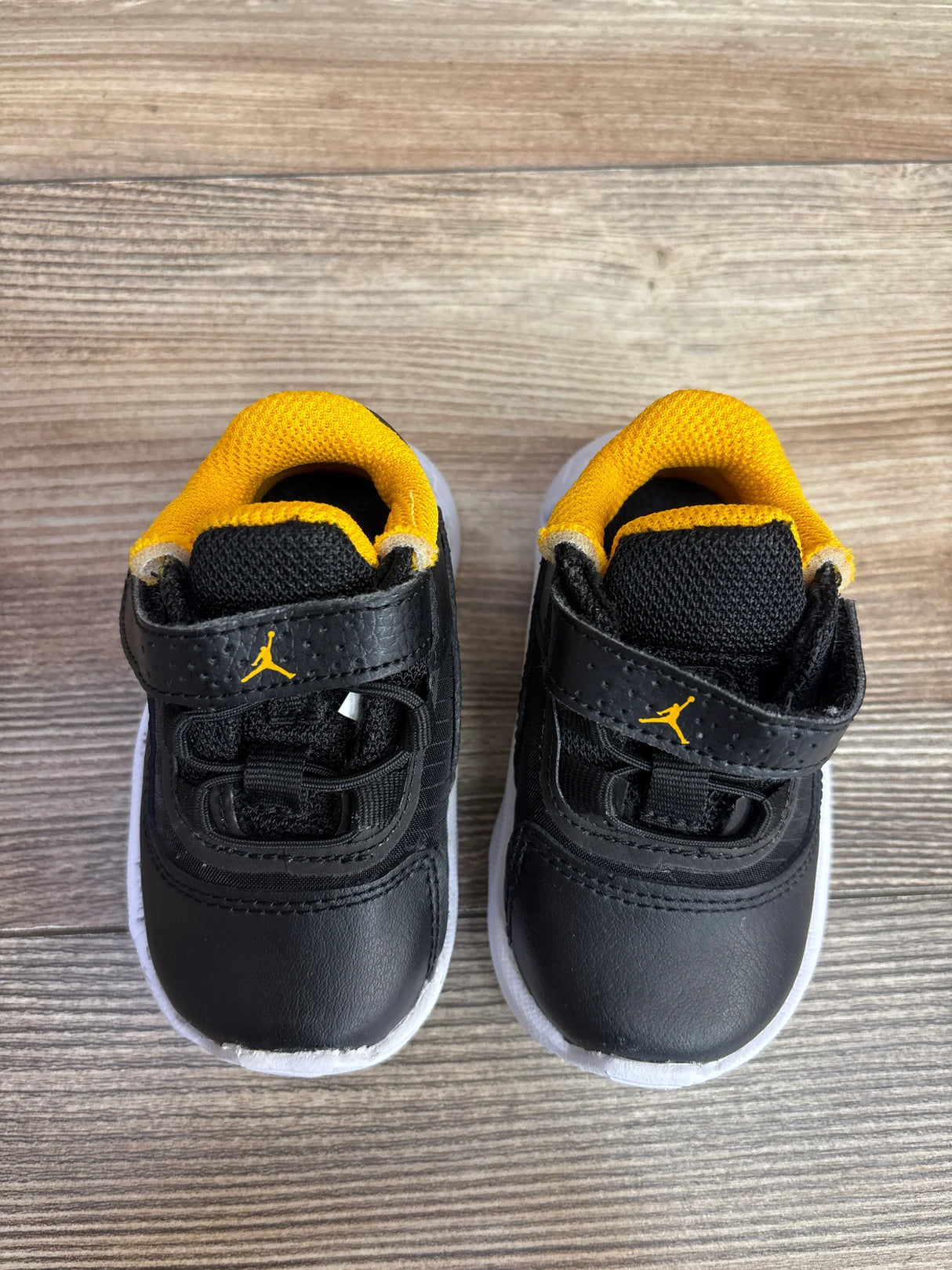 Top view of Air Jordan Black Taxi toddler sneakers with yellow lining, hook-and-loop strap, white soles on wood floor