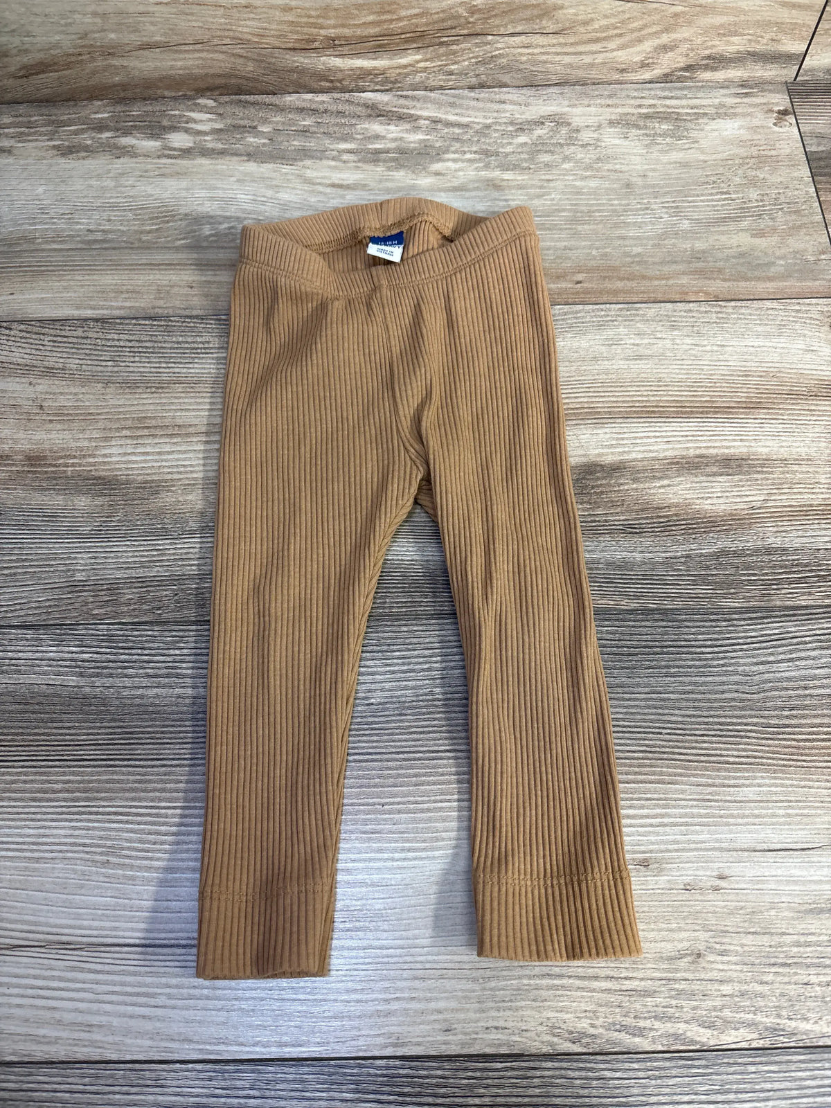 Front view of Old Navy ribbed leggings in brown, size 12 to 18 months, showcasing elastic waistband and ribbed texture with wood-grain background
