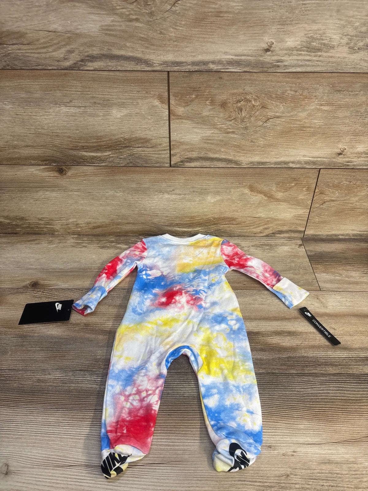 Front view of Nike infant sleeper showcasing long sleeves, footed legs, and blue, yellow, and red tie-dye on wood flooring