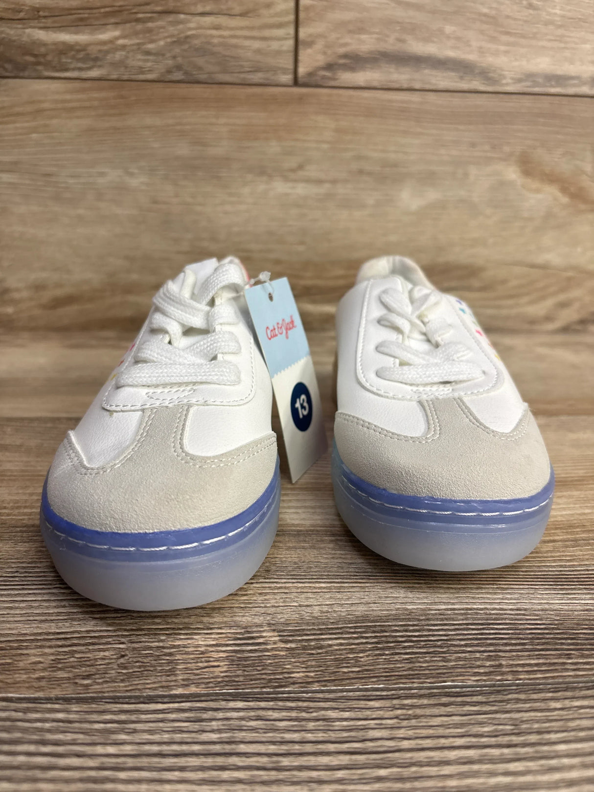 Pair of white toddler sneakers with blue soles, size 13, on wooden floor