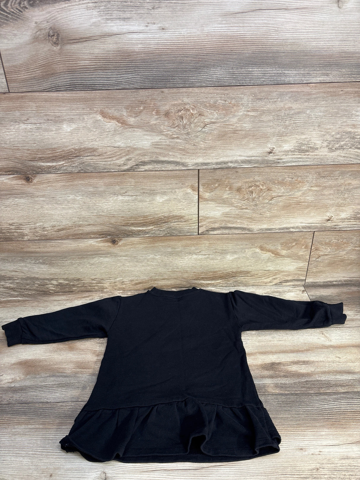Black long-sleeve toddler dress with ruffled hem on wood floor background