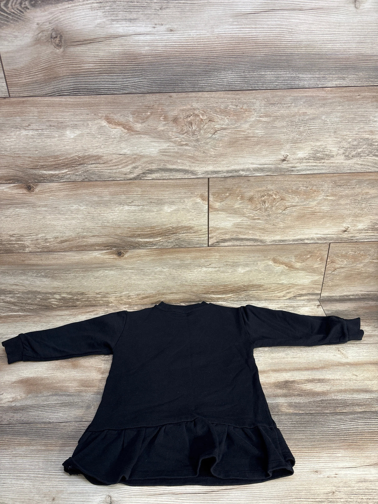 Back view of Versace black sweatshirt tunic (girls' 4T) showing long sleeves and ruffled hem on wood floor