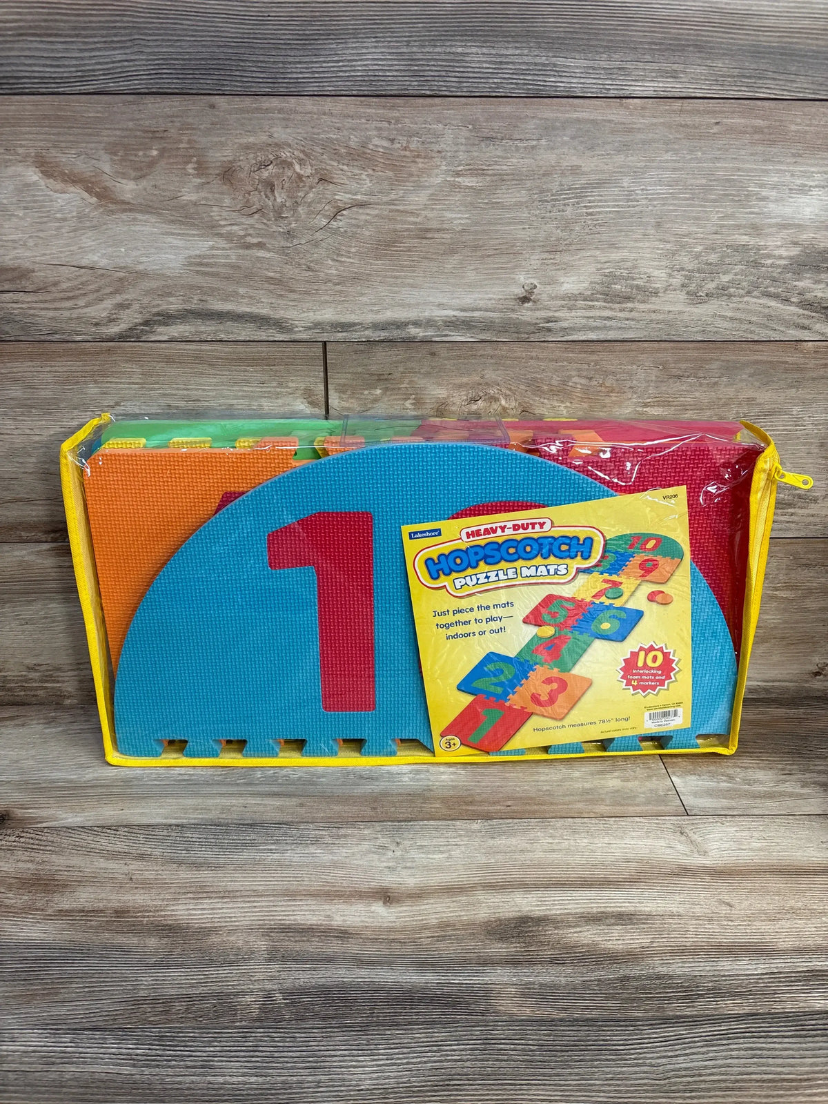 Front view of Lakeshore hopscotch puzzle mats in zippered yellow carry case, showing blue foam “1” piece on wood background