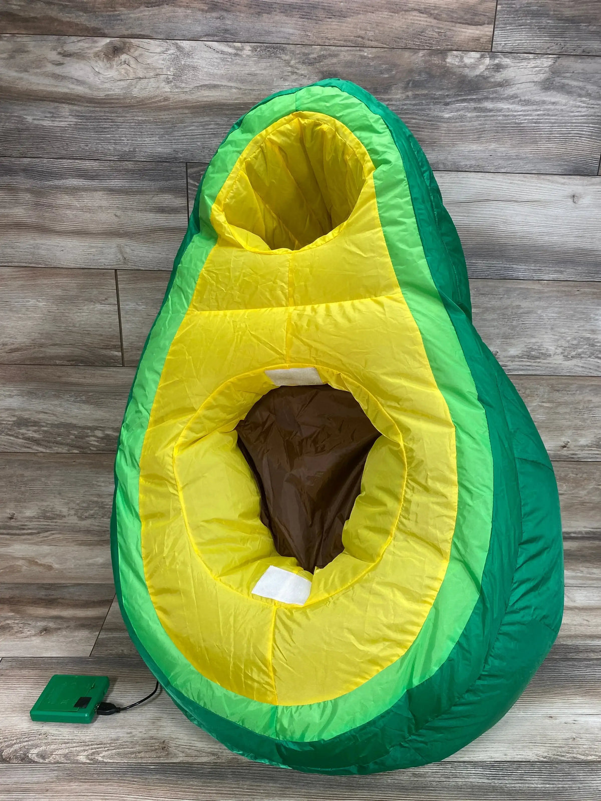Front view of green avocado inflatable costume in size 5 to 10 showcasing yellow flesh and brown pit on a wood floor