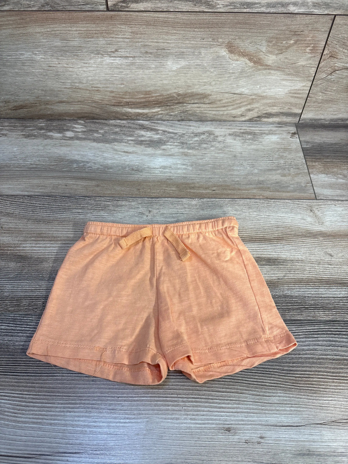 Top-down view of orange baby shorts with elastic waistband and tied drawstring, folded hem on light wood background