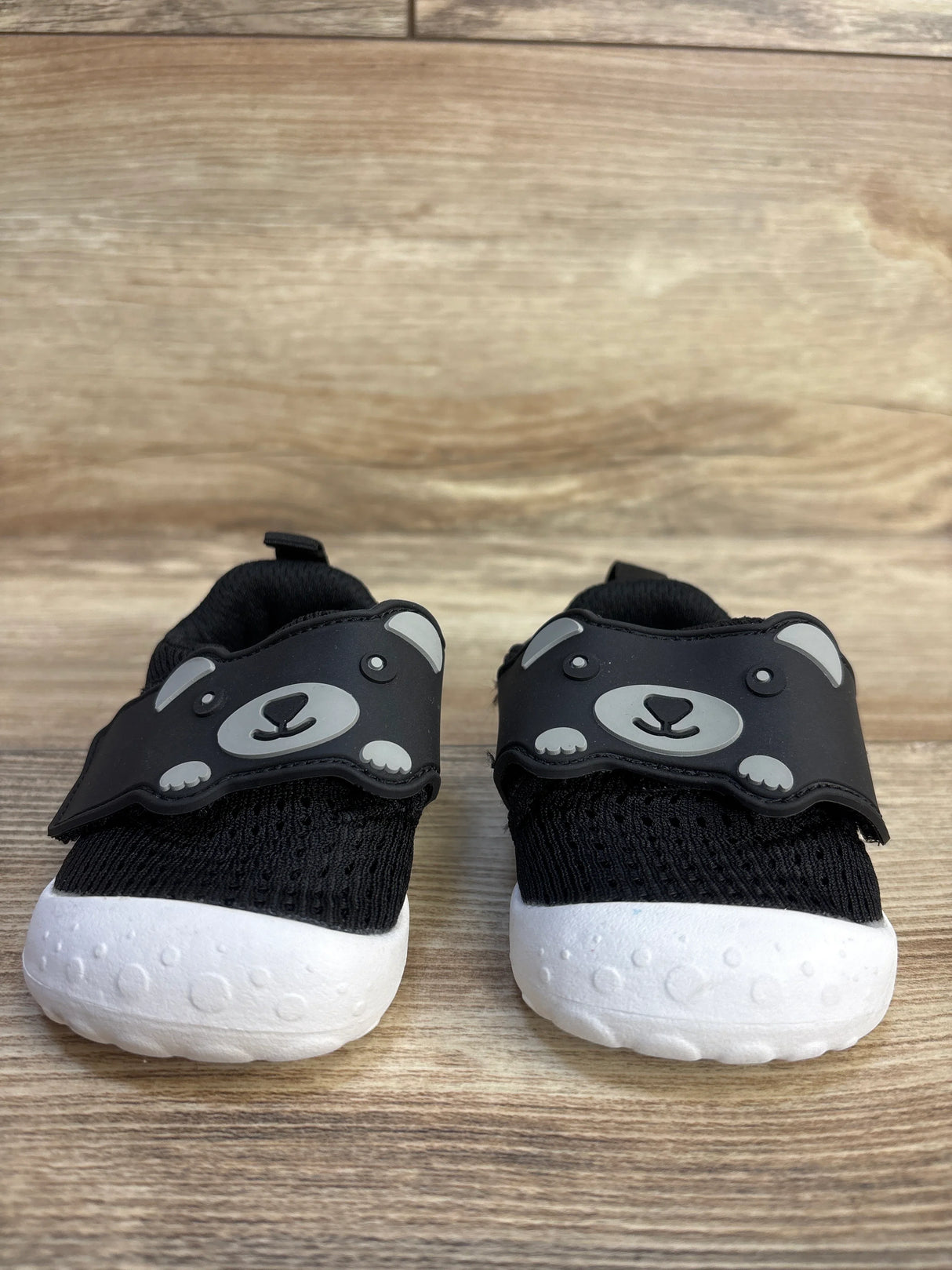 Front view of FEETCITY mesh black baby walking shoes size 4/5C showing bear-face hook-and-loop strap and white soles on wood background