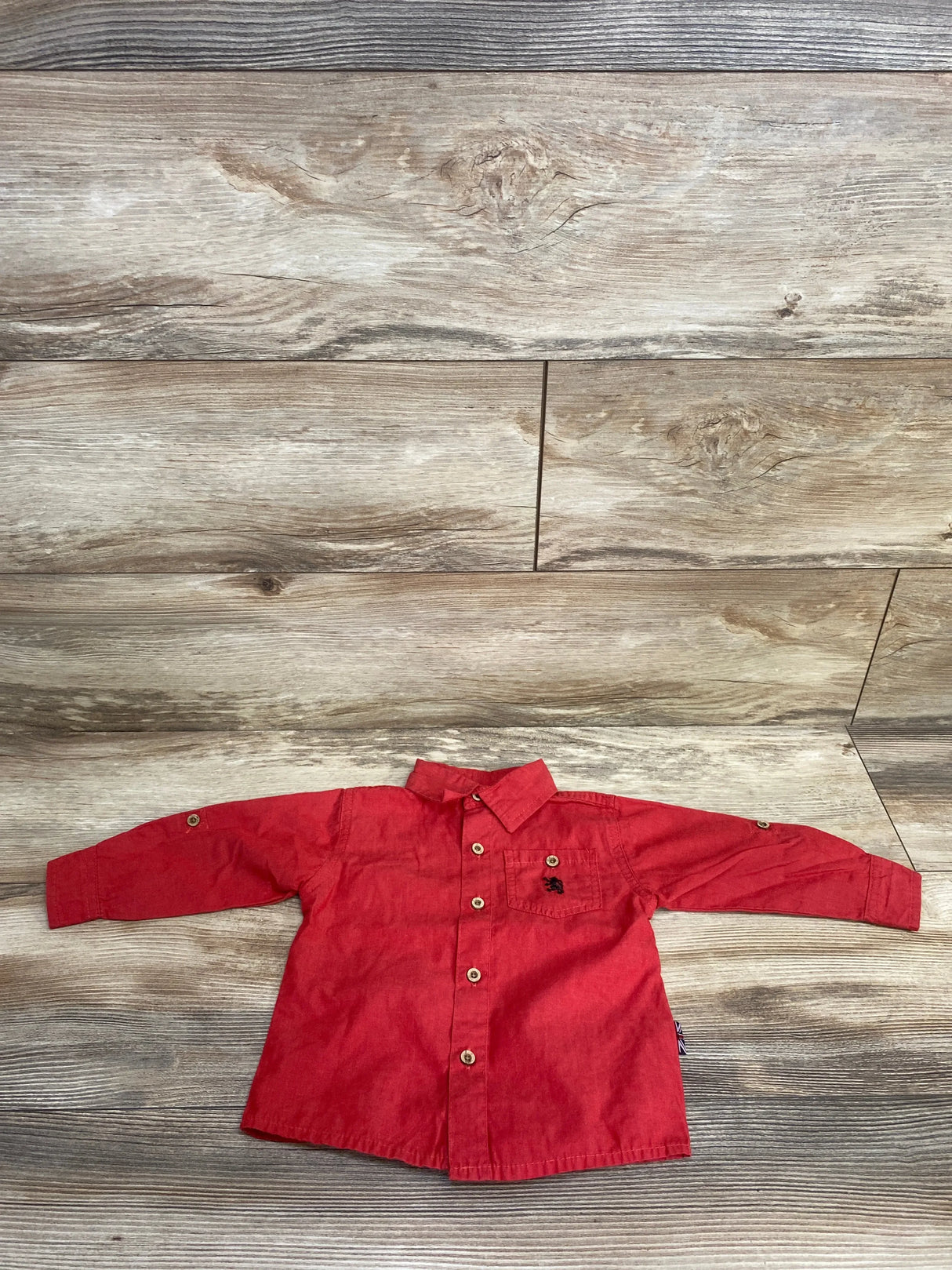 Red long-sleeve button-up toddler shirt with chest pocket on wooden background