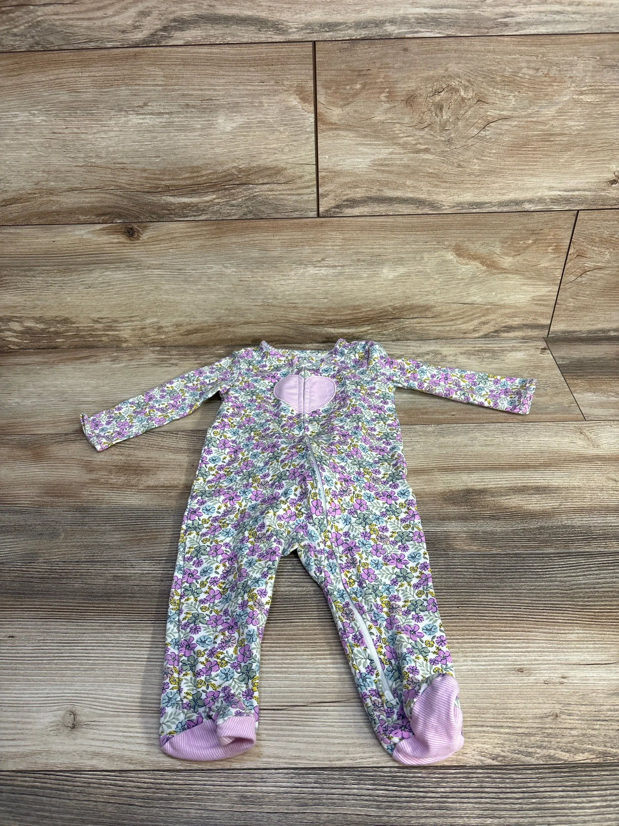 Flat lay of baby floral footed sleeper (6-9 months) showing front zipper, pink heart chest patch, and ribbed pink feet on wood background