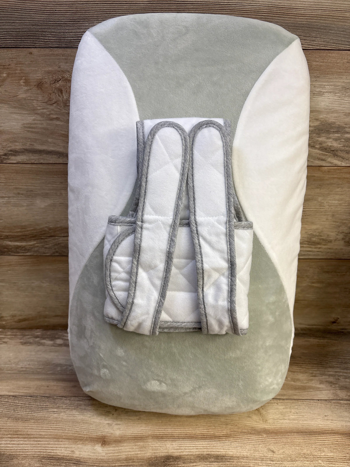 Top-down view of Babocush Newborn Comfort Cushion showing contoured gray-and-white plush pillow with quilted strap on wooden floor