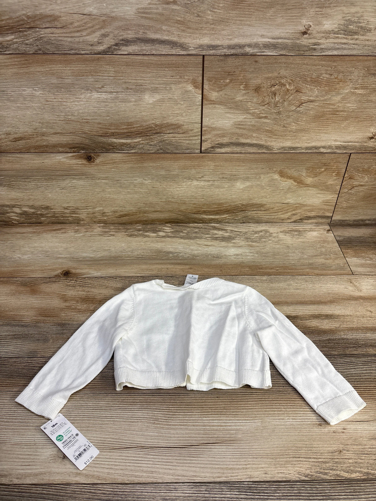 White toddler cardigan with long sleeves on wood background, price tag attached