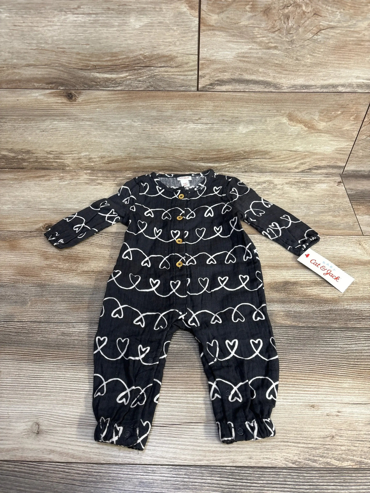 Black baby romper with white heart pattern and wooden buttons on wood floor, Cat & Jack tag