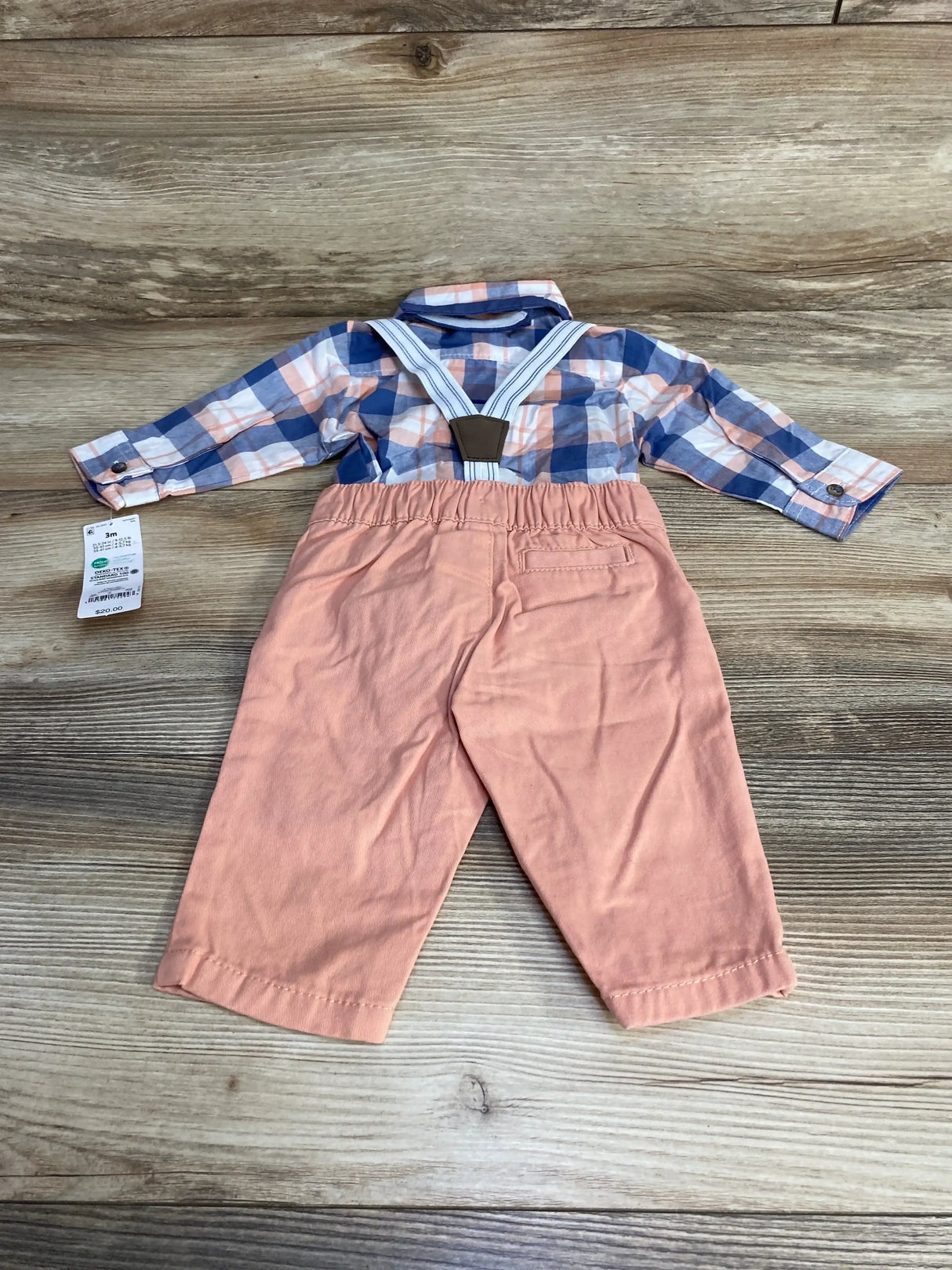 Flat lay of baby 4-piece plaid button-up shirt and peach pants with striped suspenders, size 3M tag visible on wood background