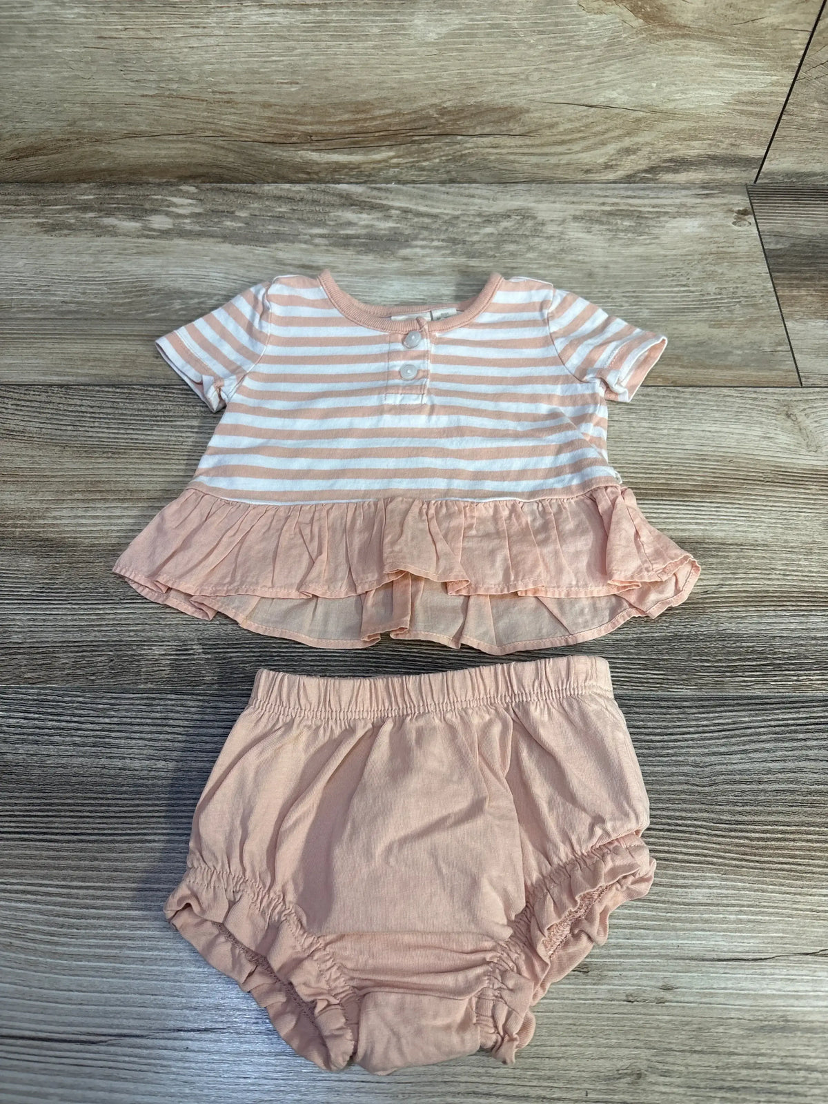 Flat lay of peach striped peplum top with ruffle hem and matching bloomers on light wood background