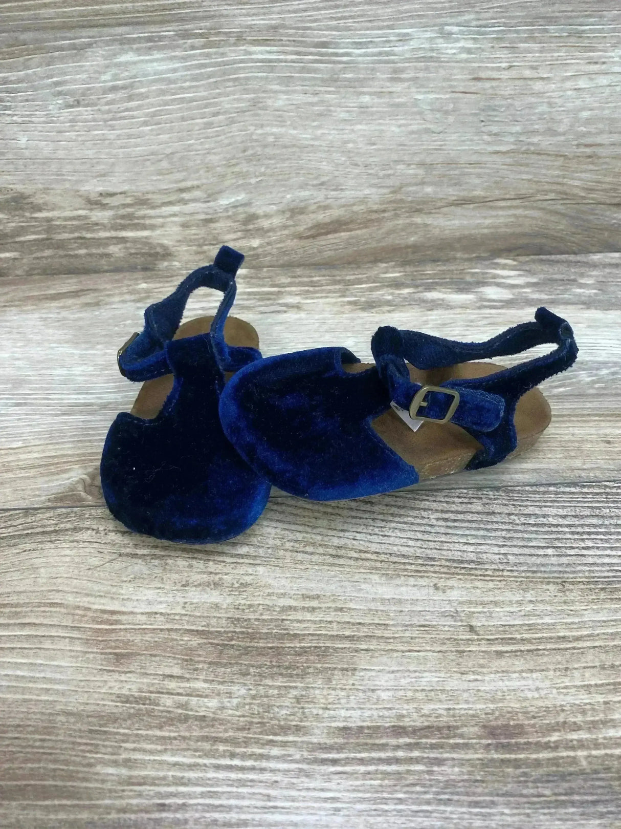 Angled front view of Baby B’gosh navy velvet sandals showing cork soles and buckle ankle straps on wood background