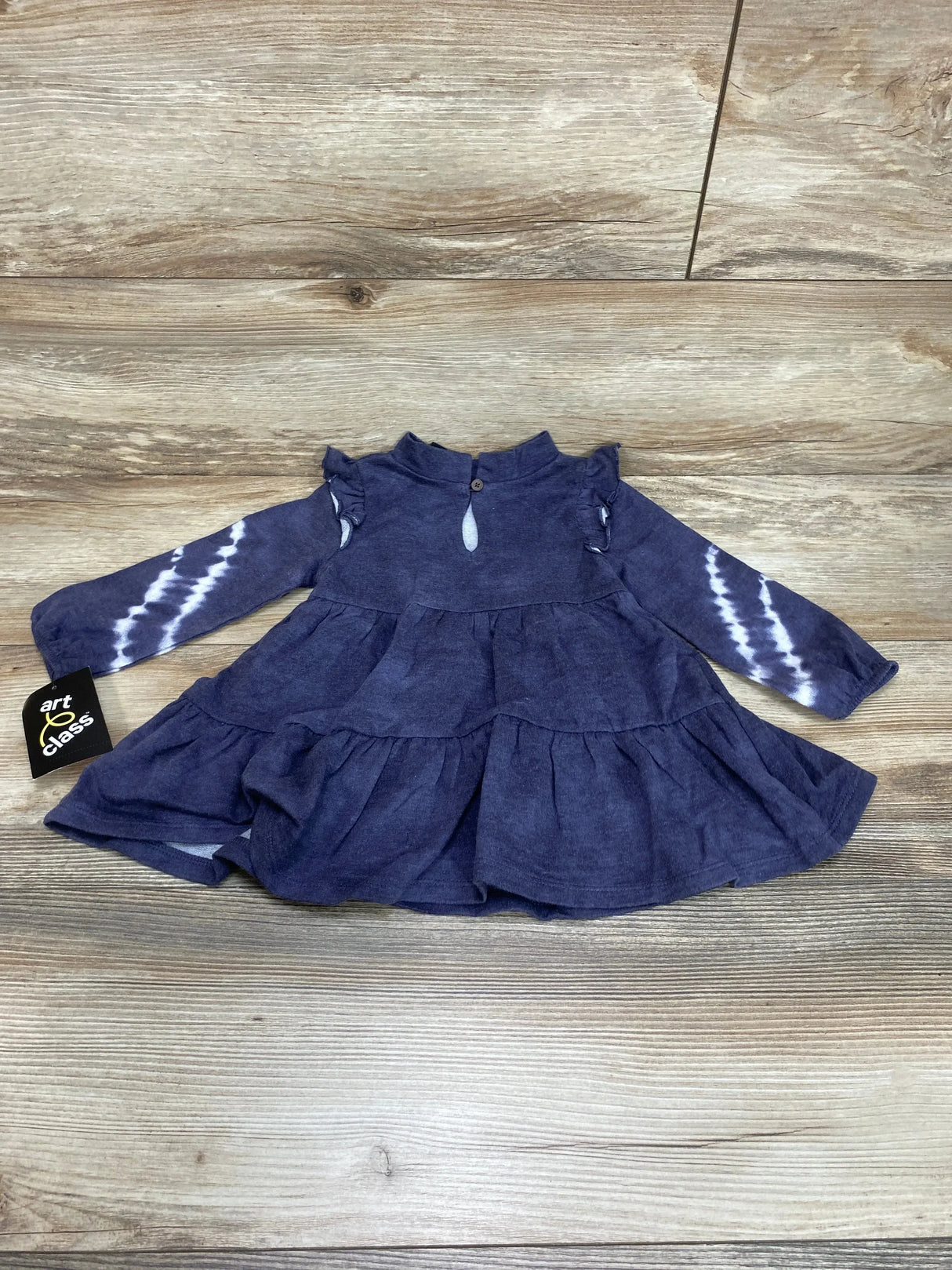 Flat lay of Art Class tiered baby dress size 12M with ruffle details, tie-dye long sleeves and keyhole button on wood