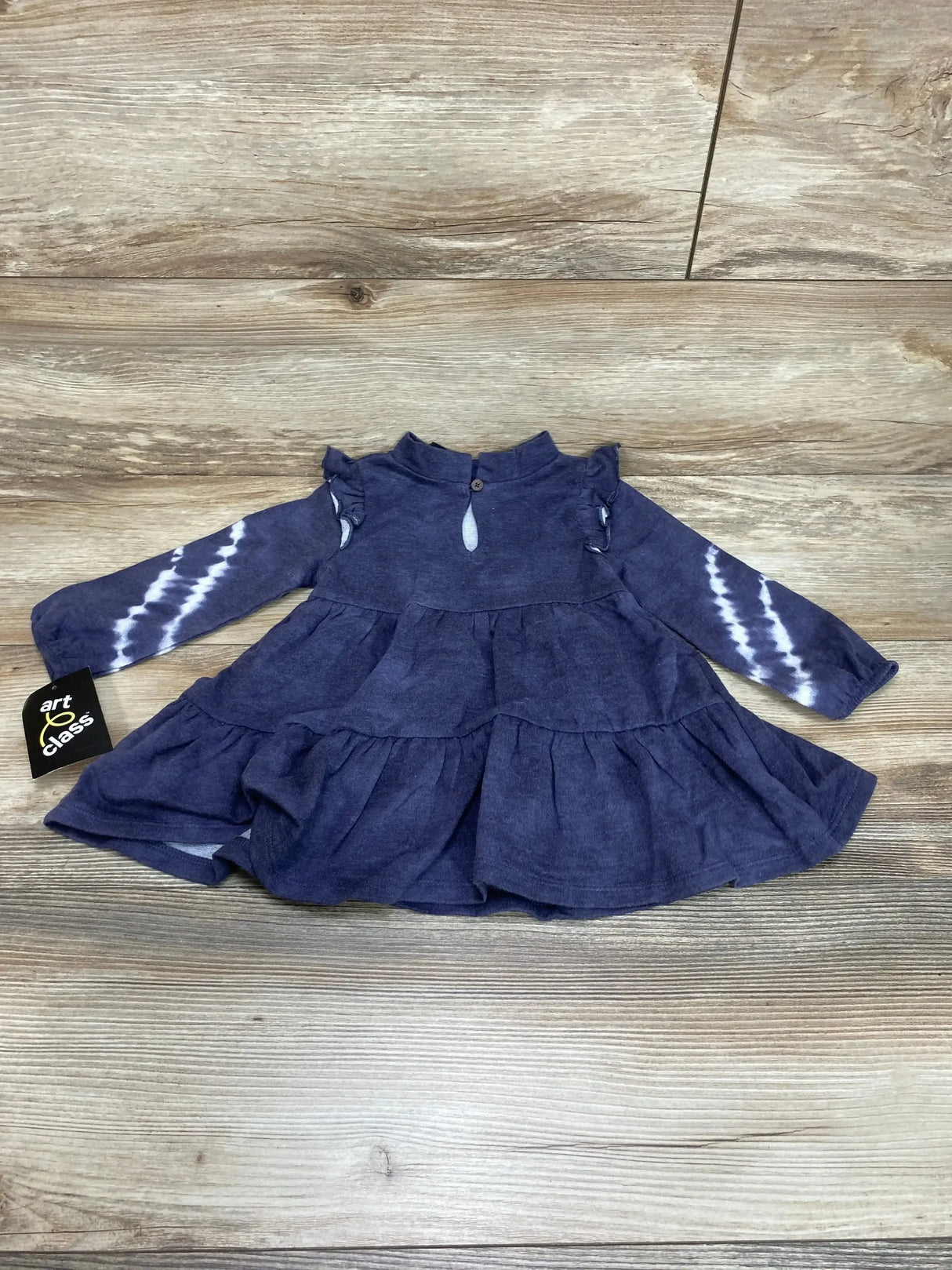 Flat lay of Art Class tiered baby dress size 12M with ruffle details, tie-dye long sleeves and keyhole button on wood