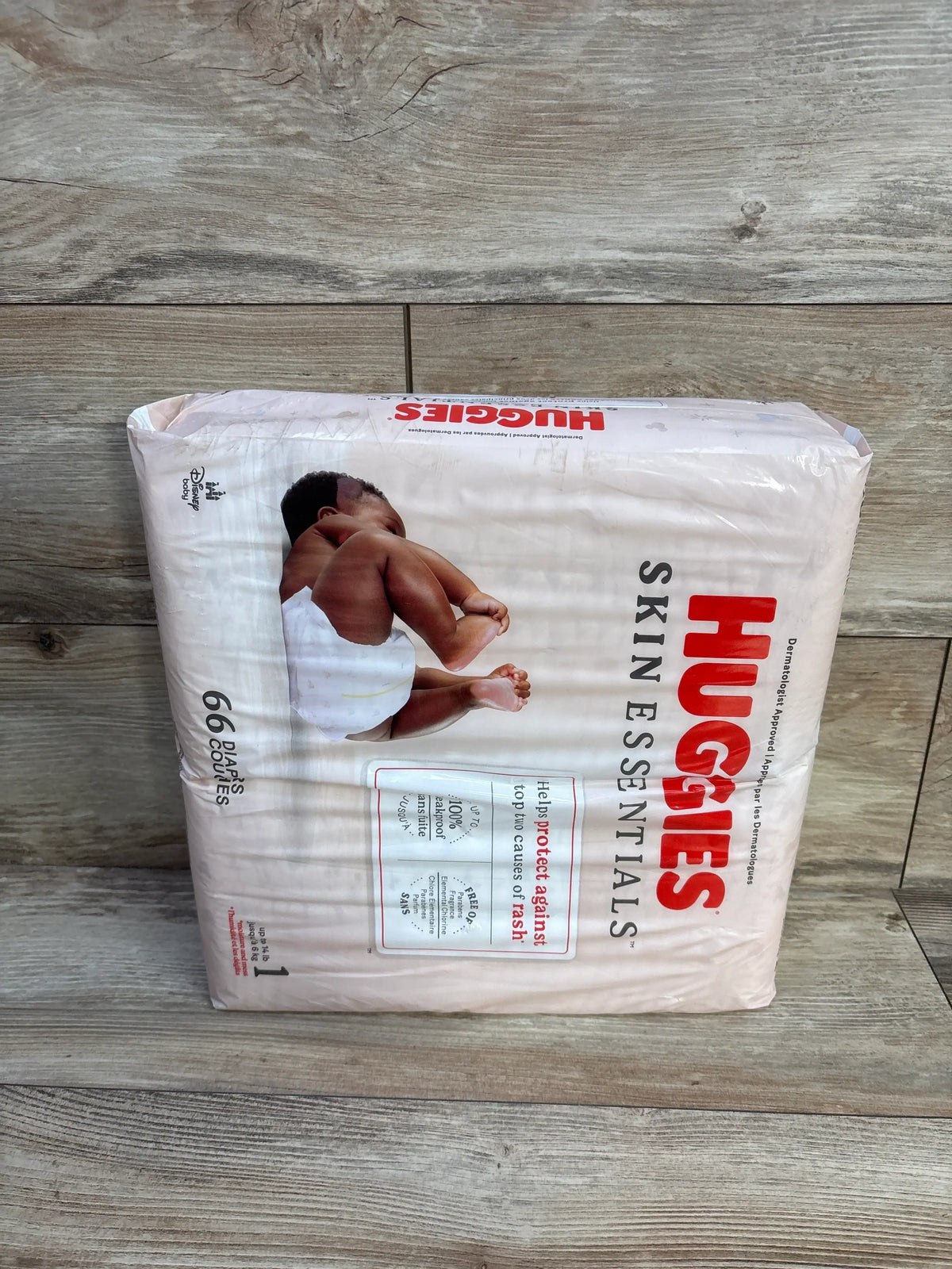 Front view of Huggies Skin Essentials diapers size 1 package showcasing rash protection and 66 diapers on a wood floor