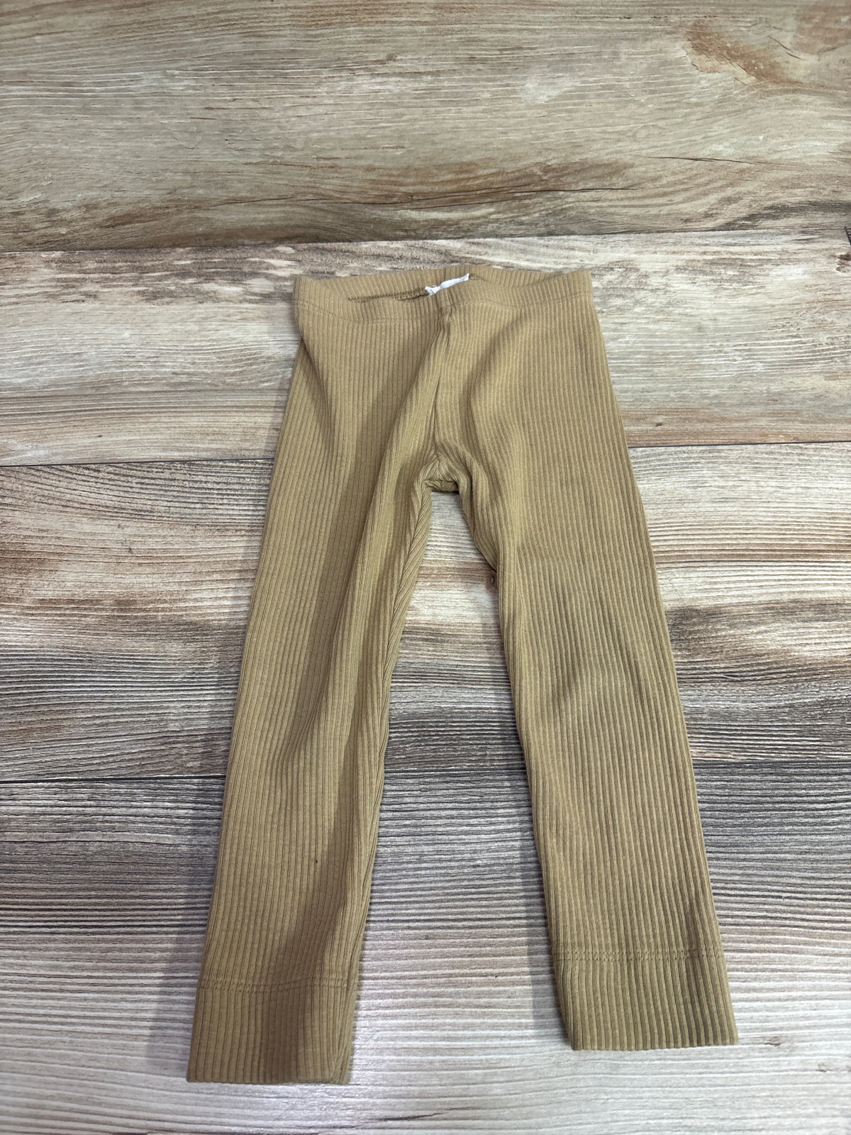 Flat-lay view of Jamie Kay caramel ribbed leggings in size 2T showcasing elastic waistband on a wood-grain surface