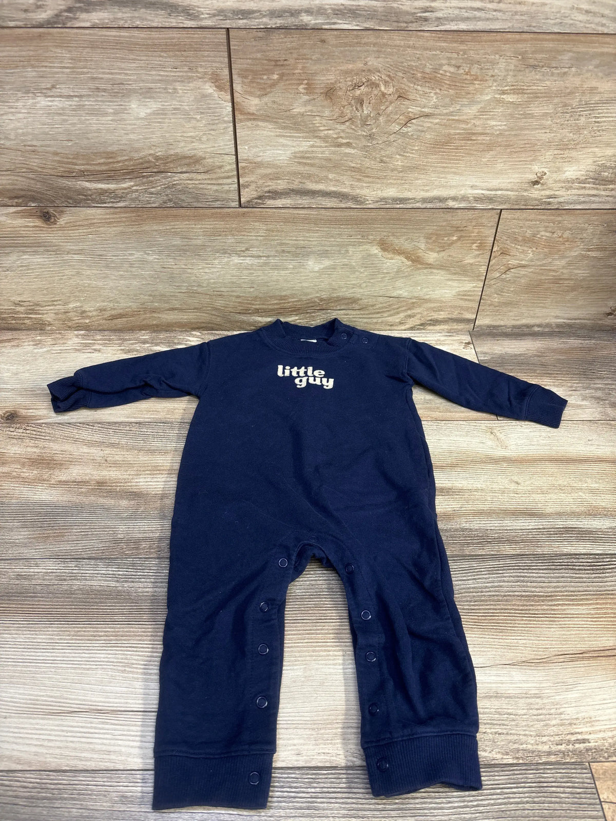 Flat-lay of navy Carter’s 12-month coverall showing little guy chest print and leg snap closures on wood floor