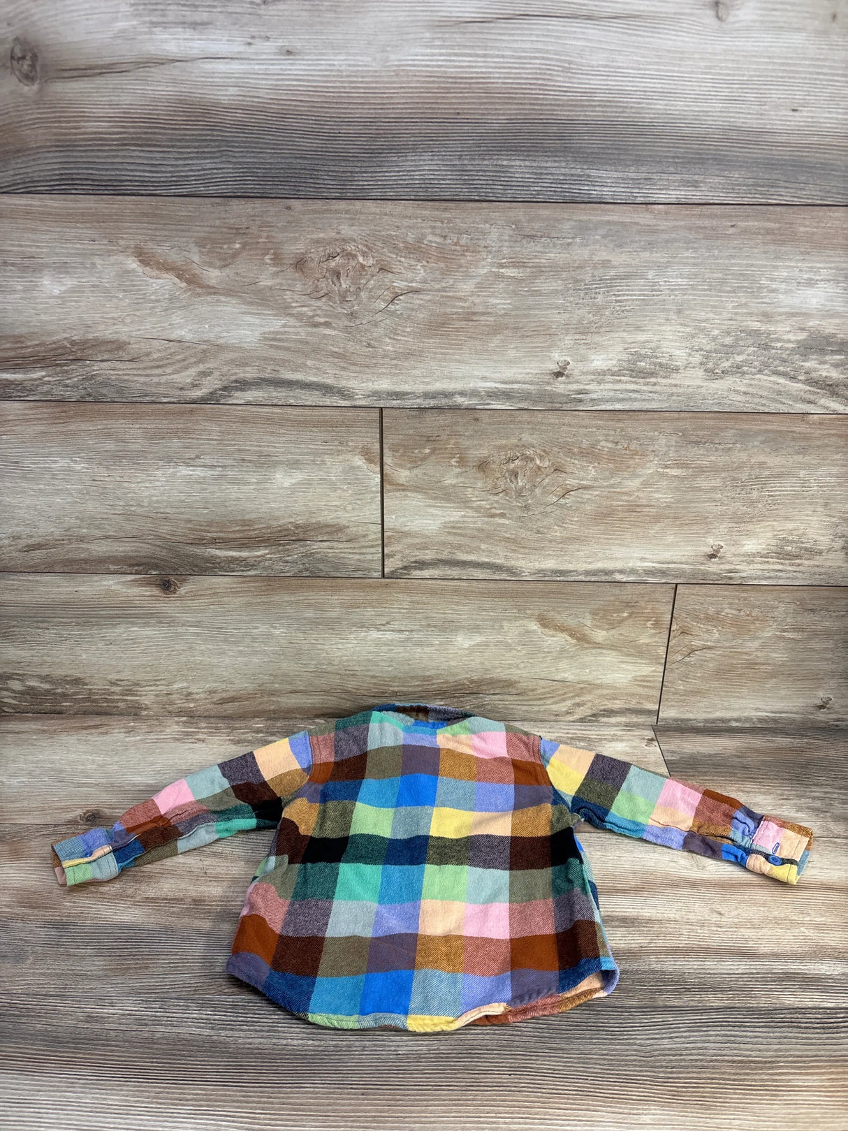 Back view of Old Navy 3T flannel button-up in multicolored check showing long sleeves and button cuffs on wood background