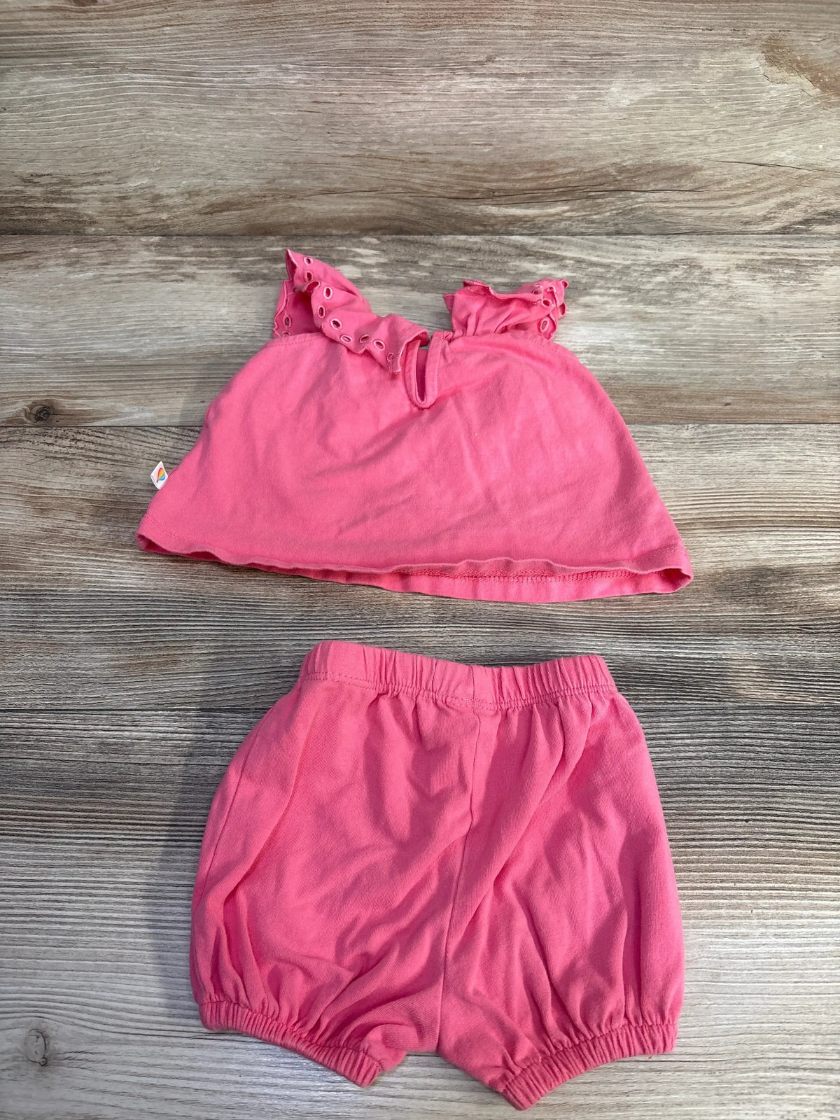 Top-down view of the pink Adventurewear 360 top and shorts set with ruffled straps and elastic-waist shorts on wood grain