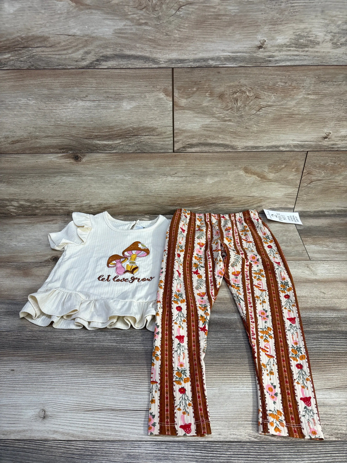 Front view of Rare Editions two piece outfit with mushroom shirt, peplum trim, and floral striped pants on wood look floor