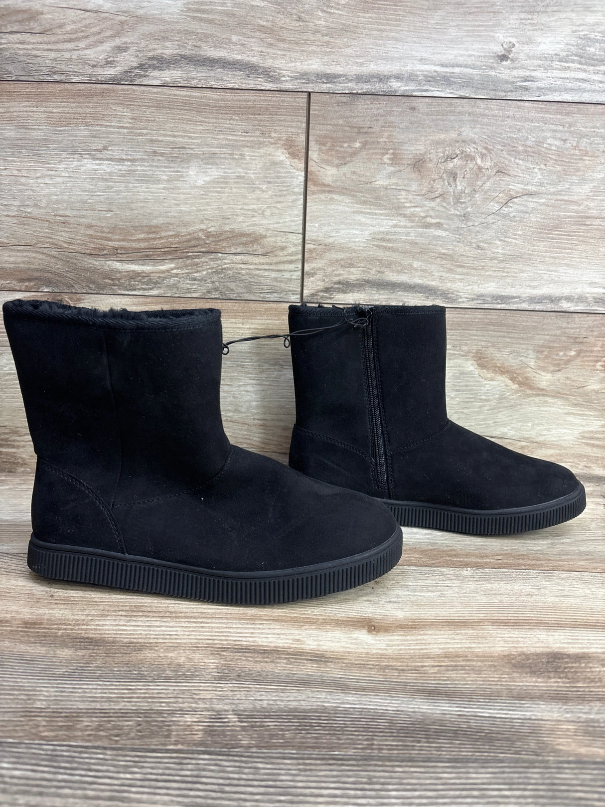 Pair of black children's winter boots with side zipper and soft lining on wood floor