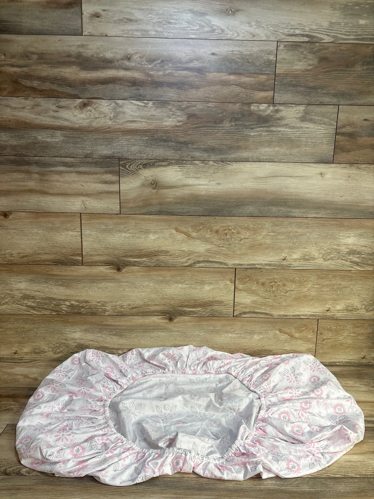 Top-down view of The Peanutshell fitted crib sheet in white with pink and gray floral print and elastic edge on wood floor
