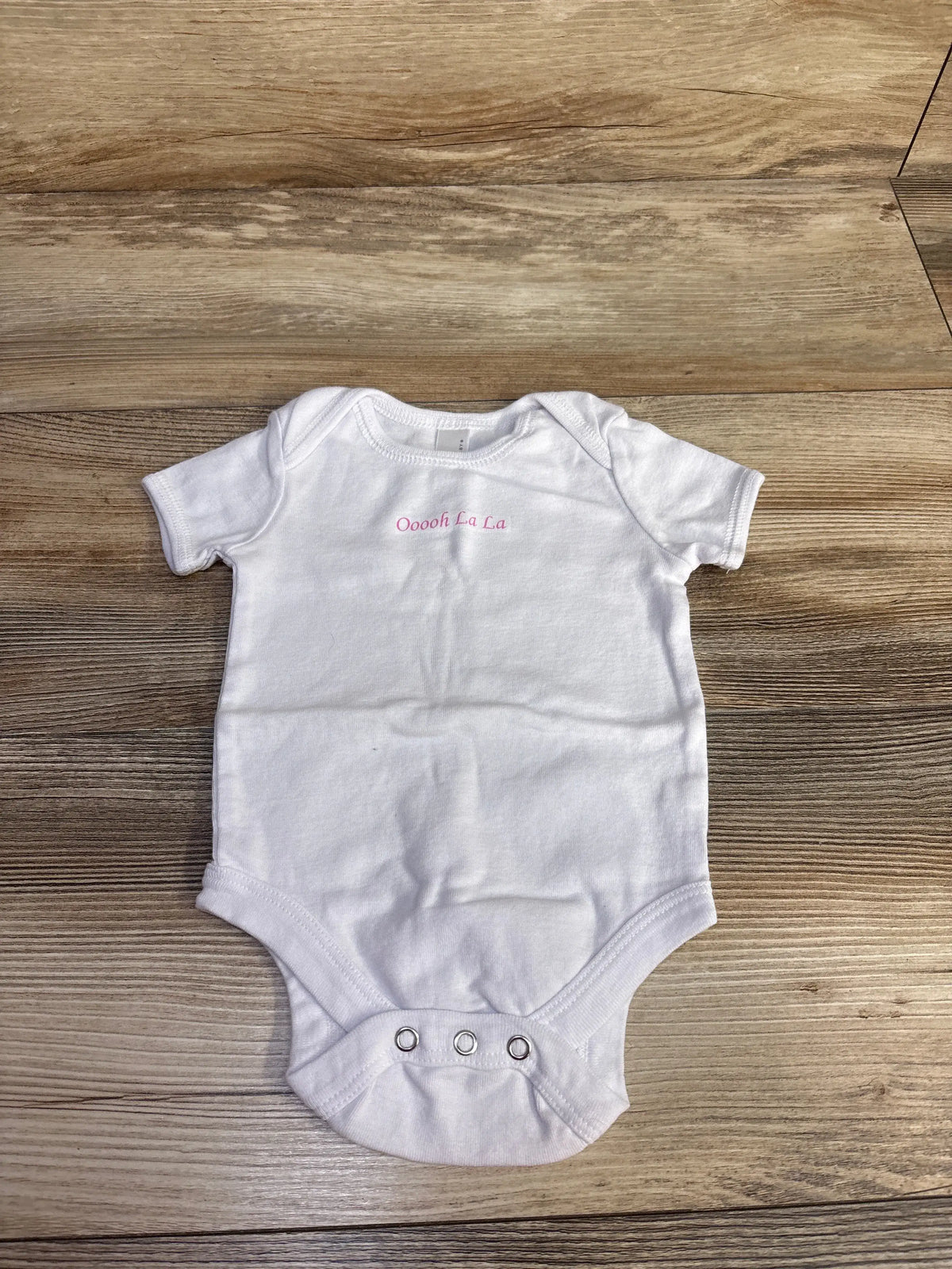 Front view of Bella Baby Ooooh La La bodysuit with white short sleeves, pink lettering, and three snaps on wood