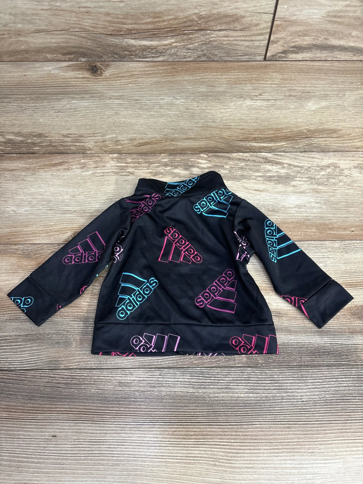 Black toddler Adidas jacket with pink and blue logo prints on wooden floor