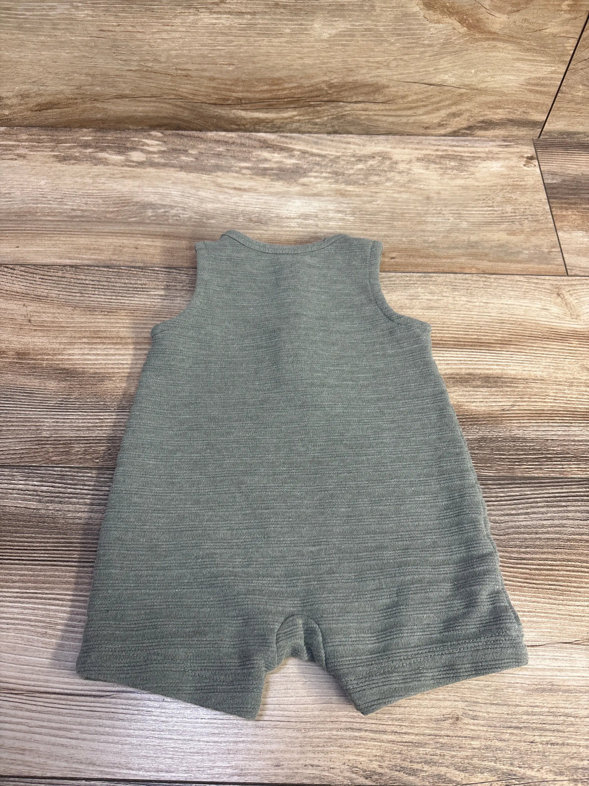 Front view of green Henley tank romper showcasing sleeveless styling, ribbed texture, and shorts on a wood-grain background